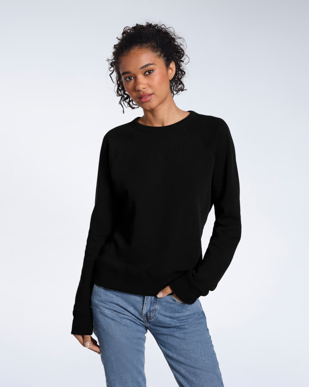 A woman looking into the camera with a hand in her pocket, modelling a plain black french terry organic cotton sweatshirt.
