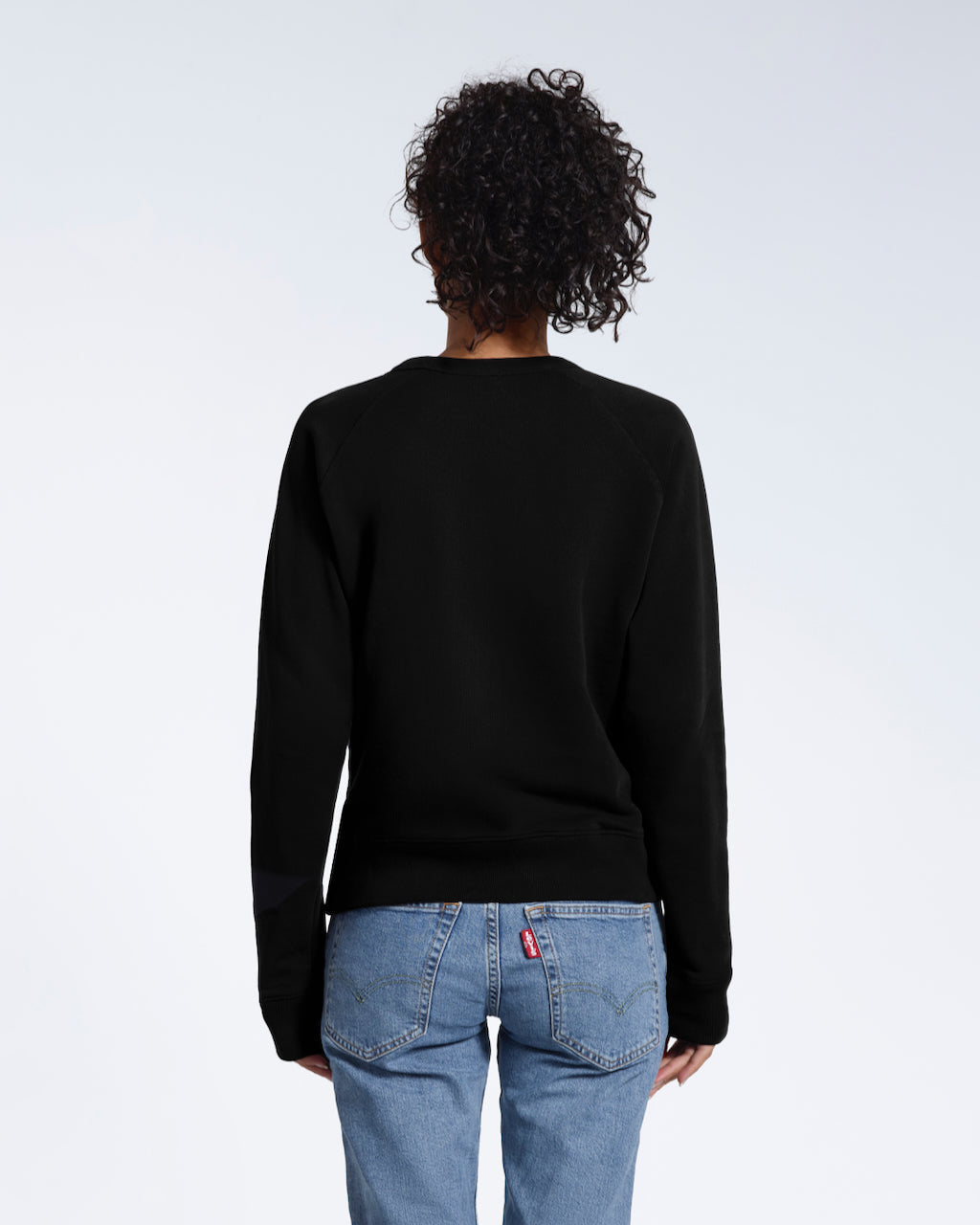 A woman facing away from the camera, showing the back of her plain black french terry organic cotton sweatshirt.