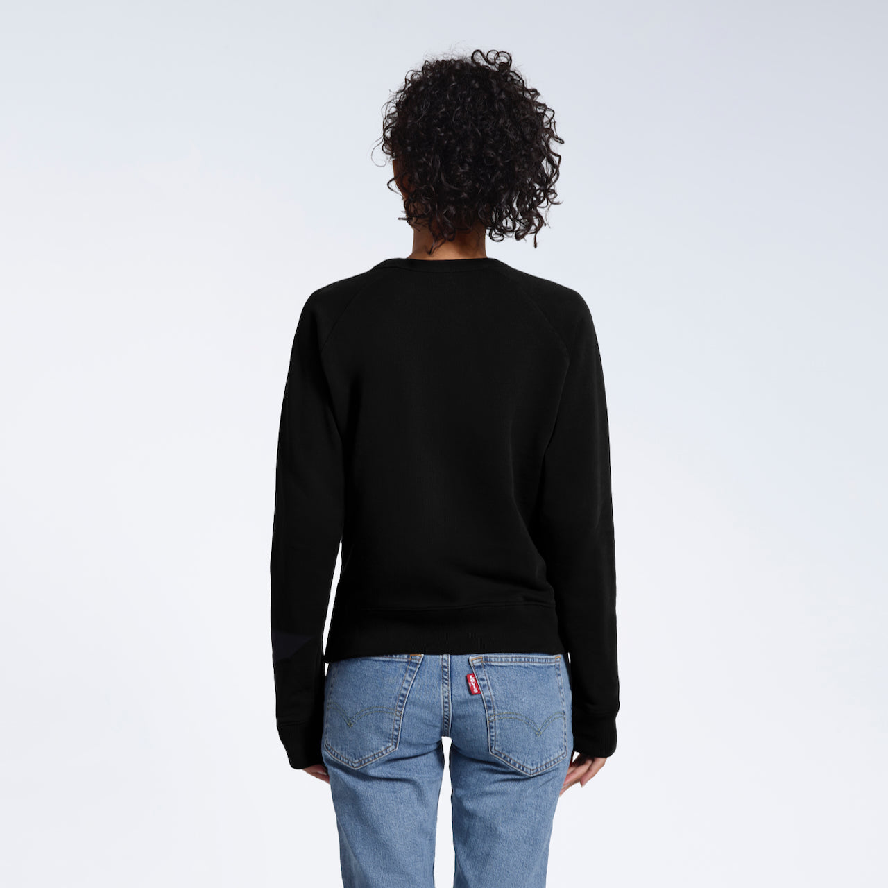 A woman facing away from the camera, showing the back of her plain black french terry organic cotton sweatshirt.
