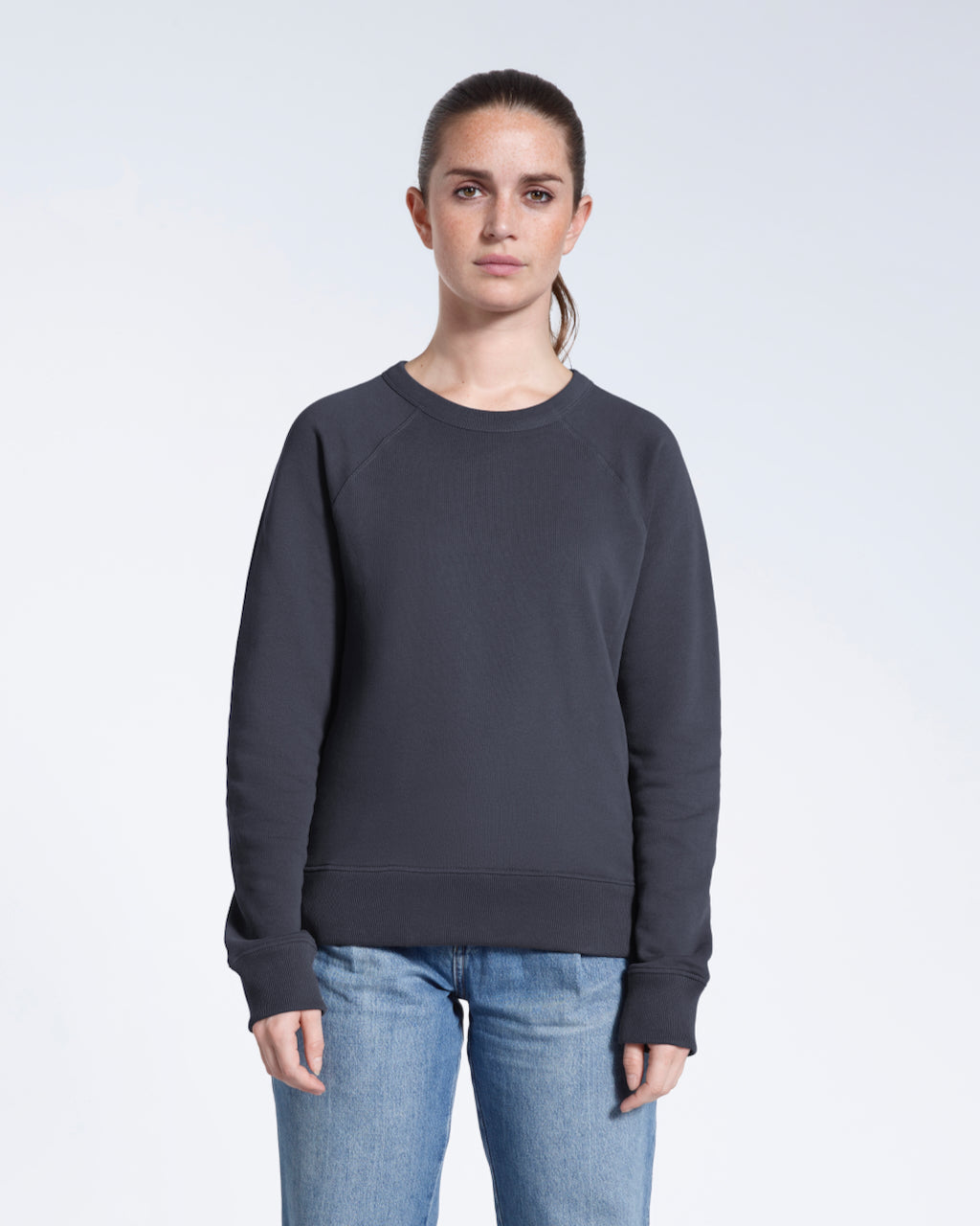 A woman face on looking into the camera with her arms by her side, modelling a plain dark grey french terry organic cotton sweatshirt.