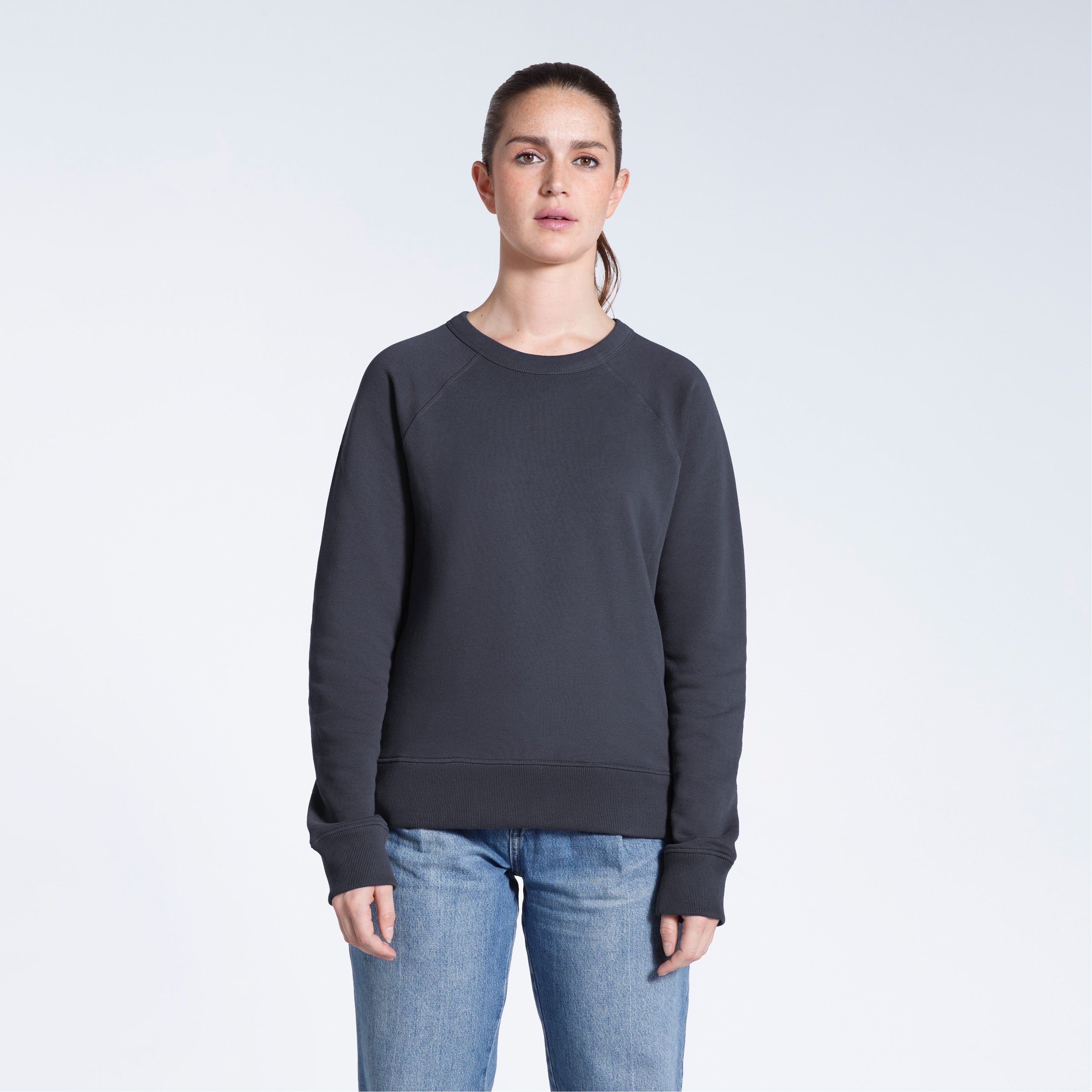 A woman face on looking into the camera with her arms by her side, modelling a plain dark grey french terry organic cotton sweatshirt.