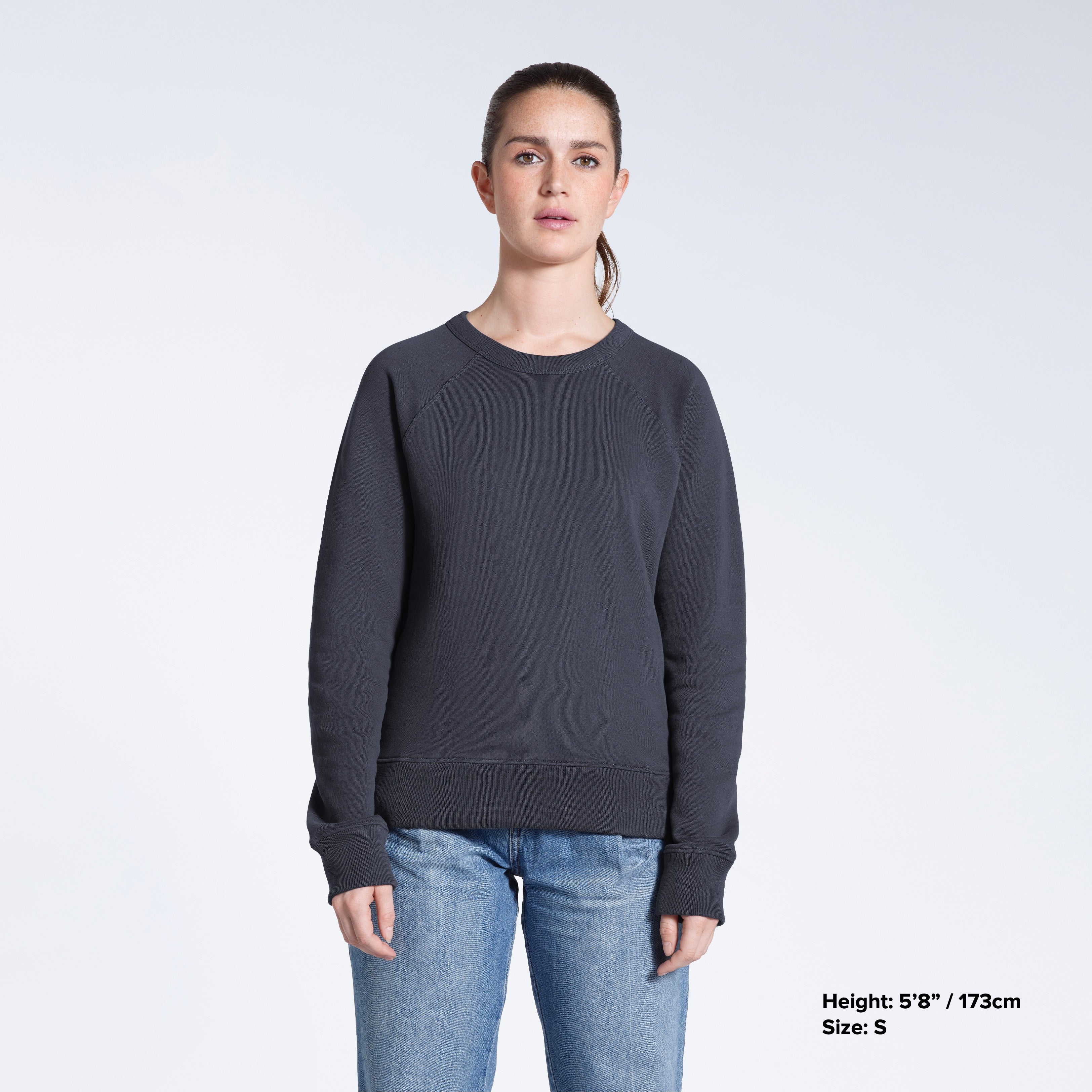 A woman face on looking into the camera with her arms by her side, modelling a plain dark grey french terry organic cotton sweatshirt.