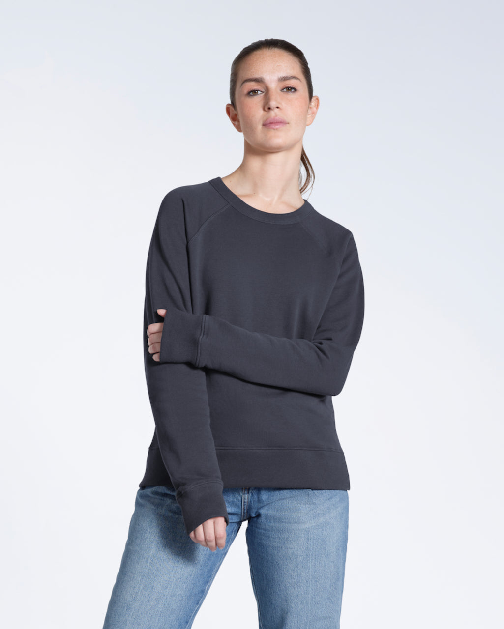 A woman looking into the camera touching her arm, modelling a plain dark grey french terry organic cotton sweatshirt.