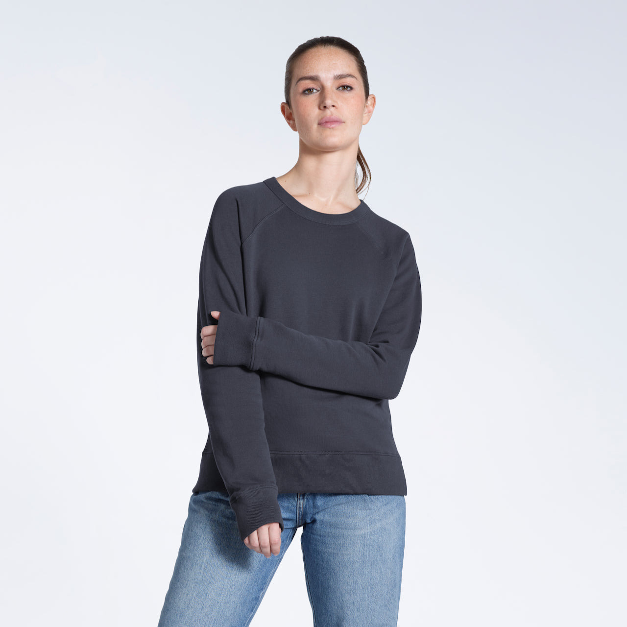 A woman looking into the camera touching her arm, modelling a plain dark grey french terry organic cotton sweatshirt.