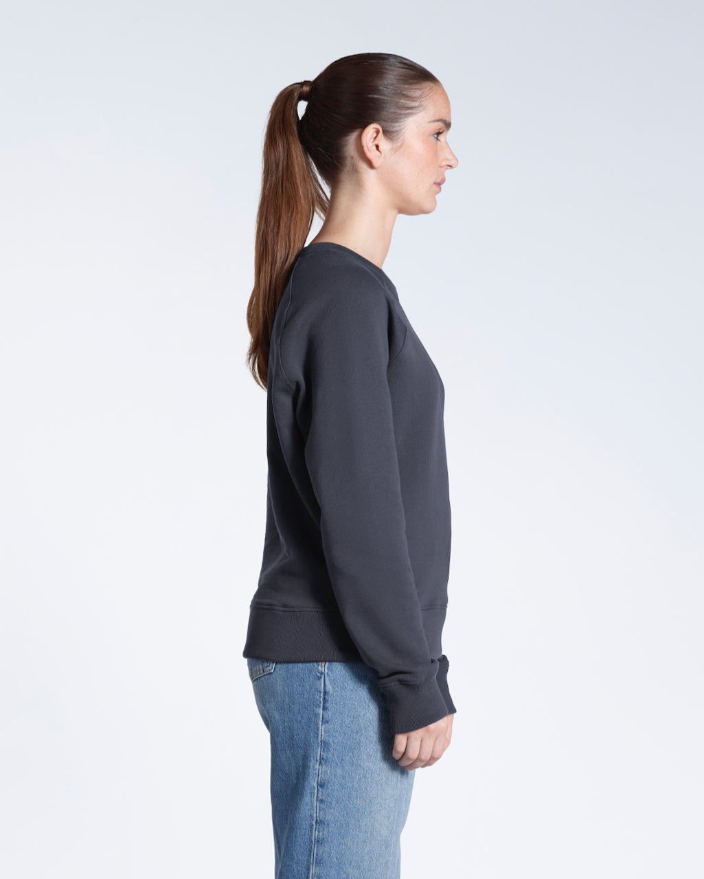 A woman facing side on, modelling a plain dark grey french terry organic cotton sweatshirt.