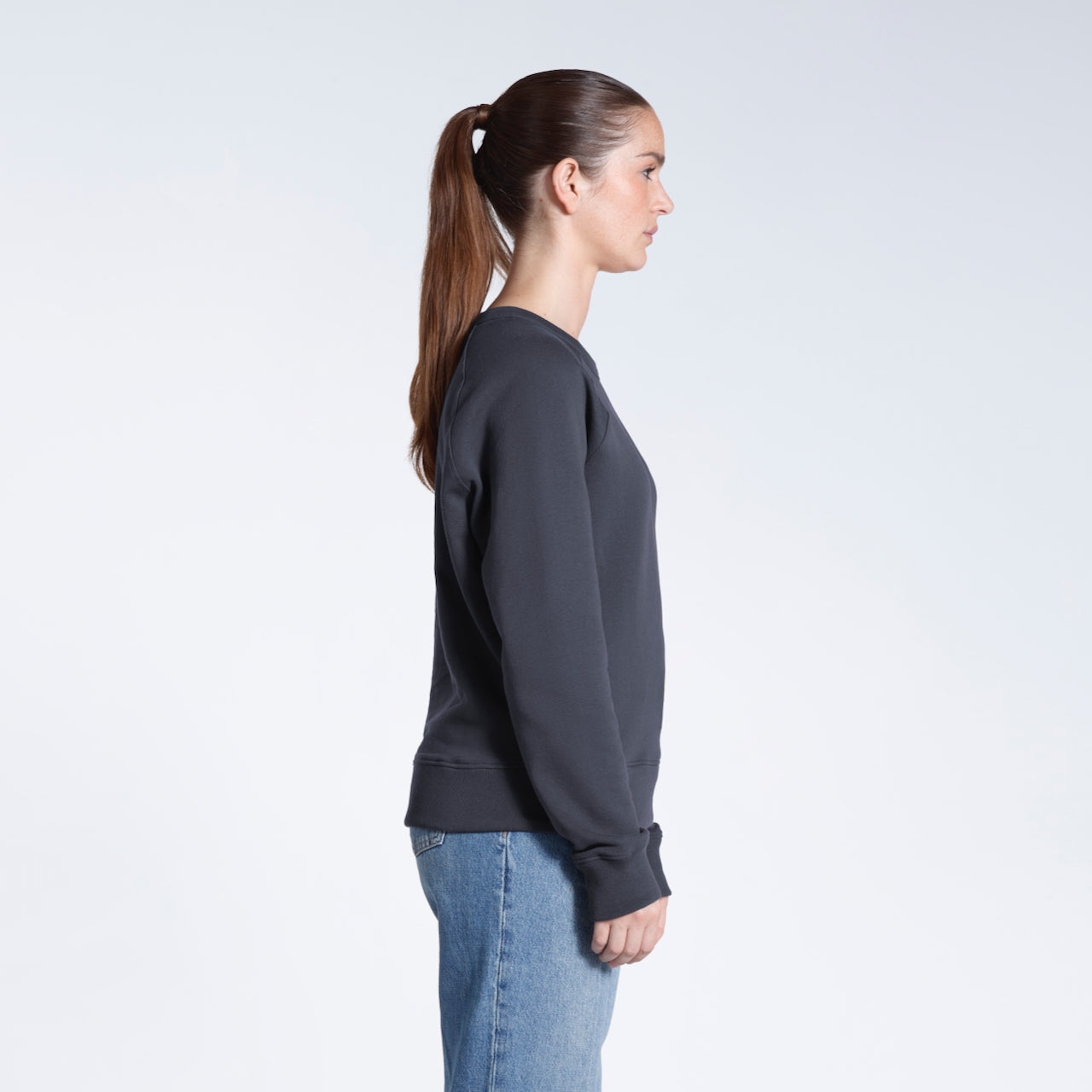A woman facing side on, modelling a plain dark grey french terry organic cotton sweatshirt.
