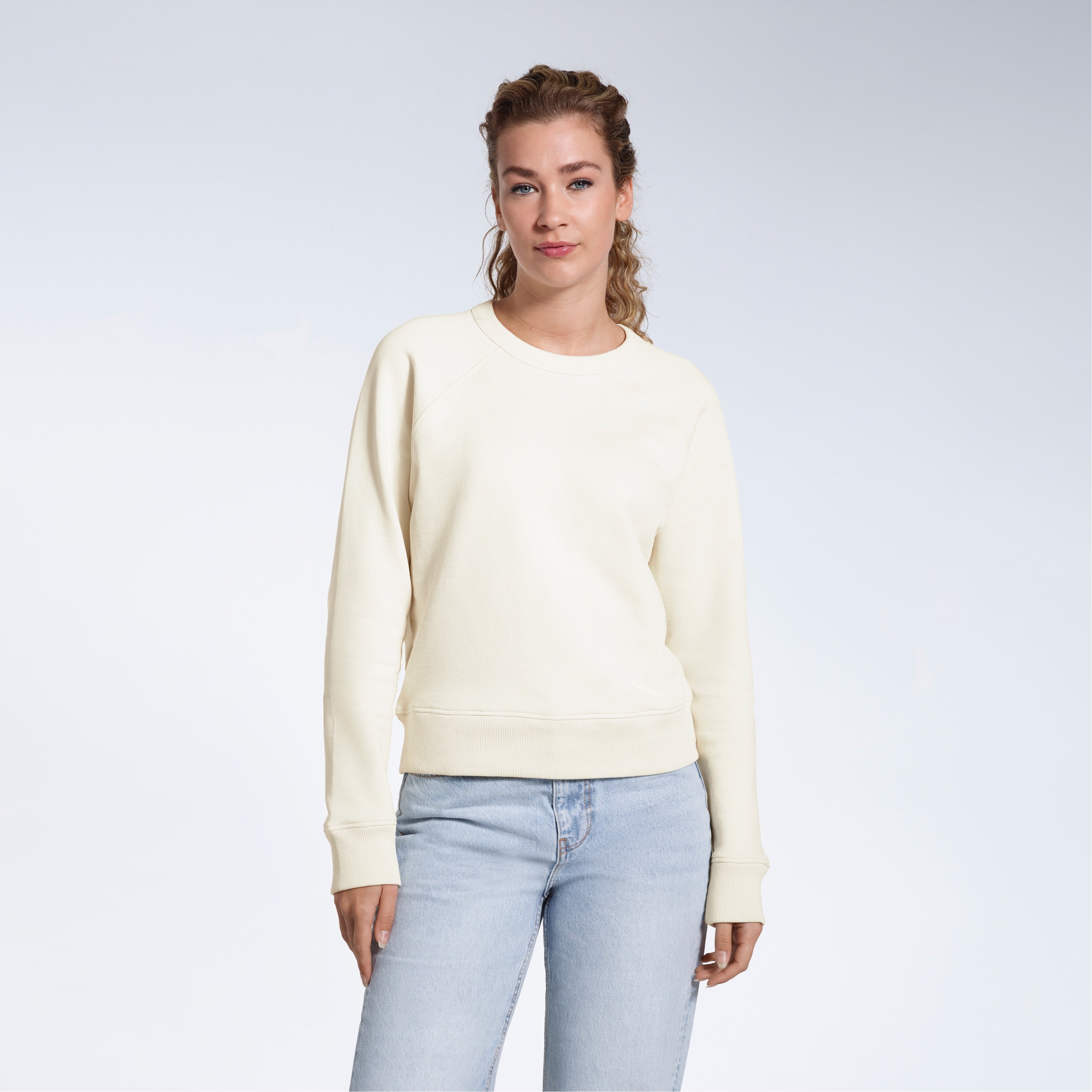 A woman face on looking into the camera with her arms by her side, modelling a plain ecru french terry organic cotton sweatshirt.
