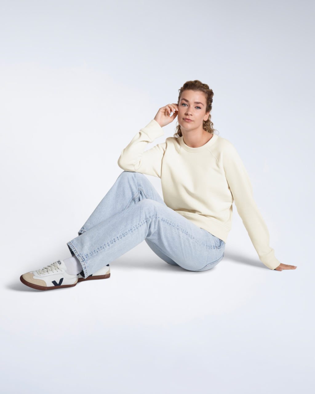 A woman sitting on the floor looking into the camera, modelling a plain ecru french terry organic cotton sweatshirt.