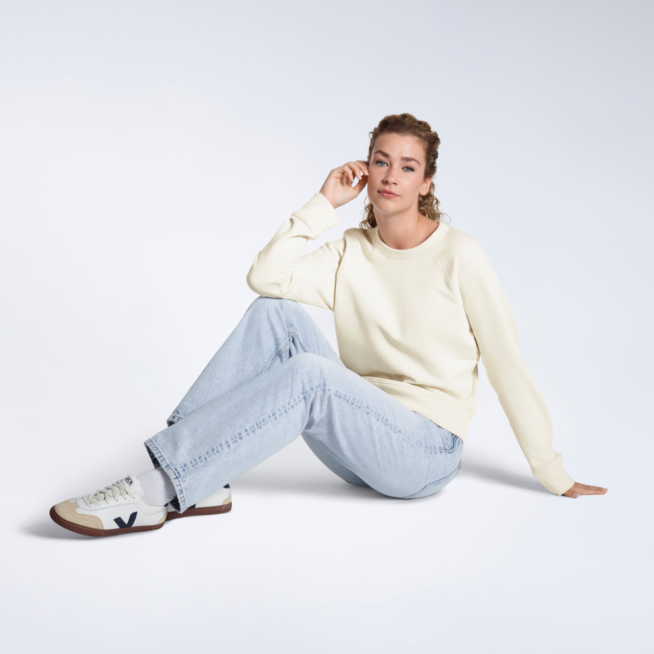 A woman sitting on the floor looking into the camera, modelling a plain ecru french terry organic cotton sweatshirt.