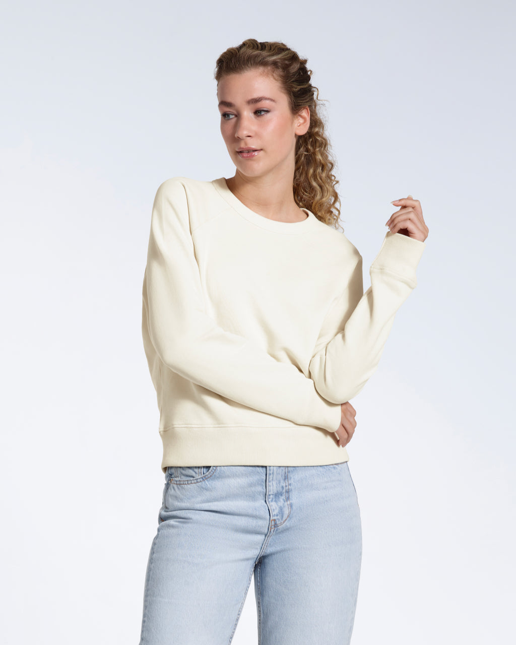 A woman looking away from the camera, modelling a plain ecru french terry organic cotton sweatshirt.