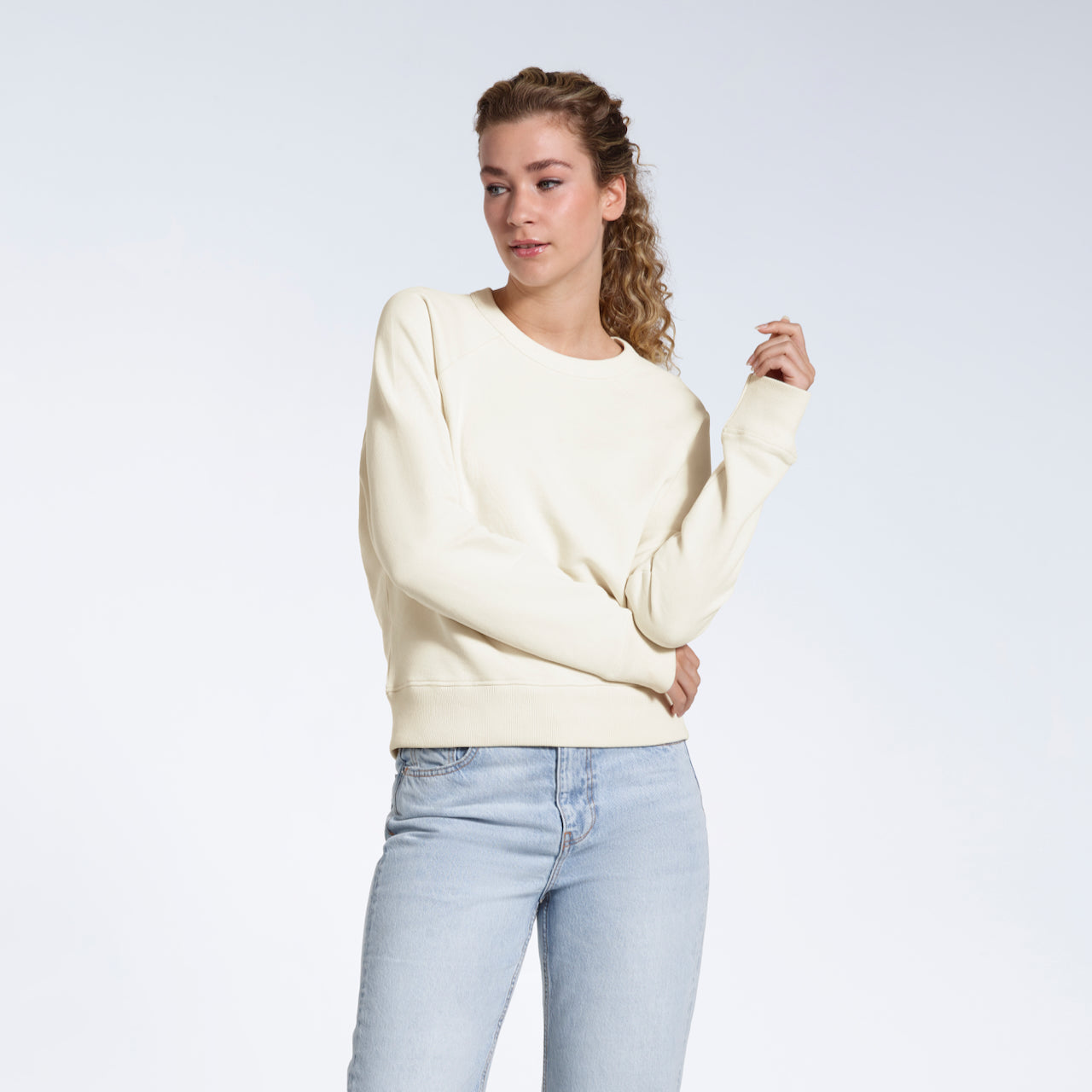 A woman looking away from the camera, modelling a plain ecru french terry organic cotton sweatshirt.