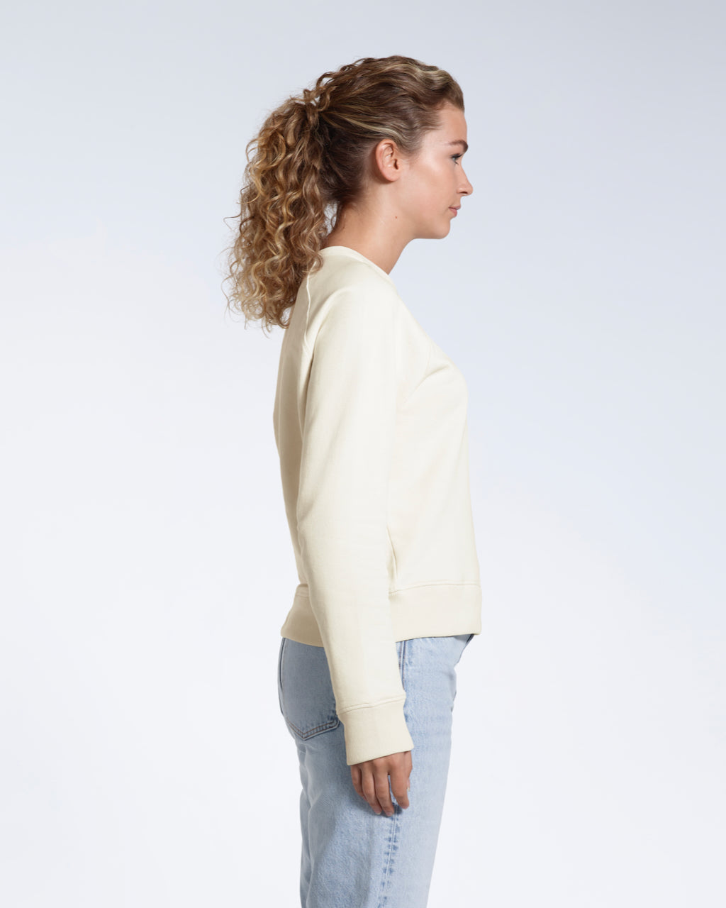 A woman facing side on, modelling a plain ecru french terry organic cotton sweatshirt.