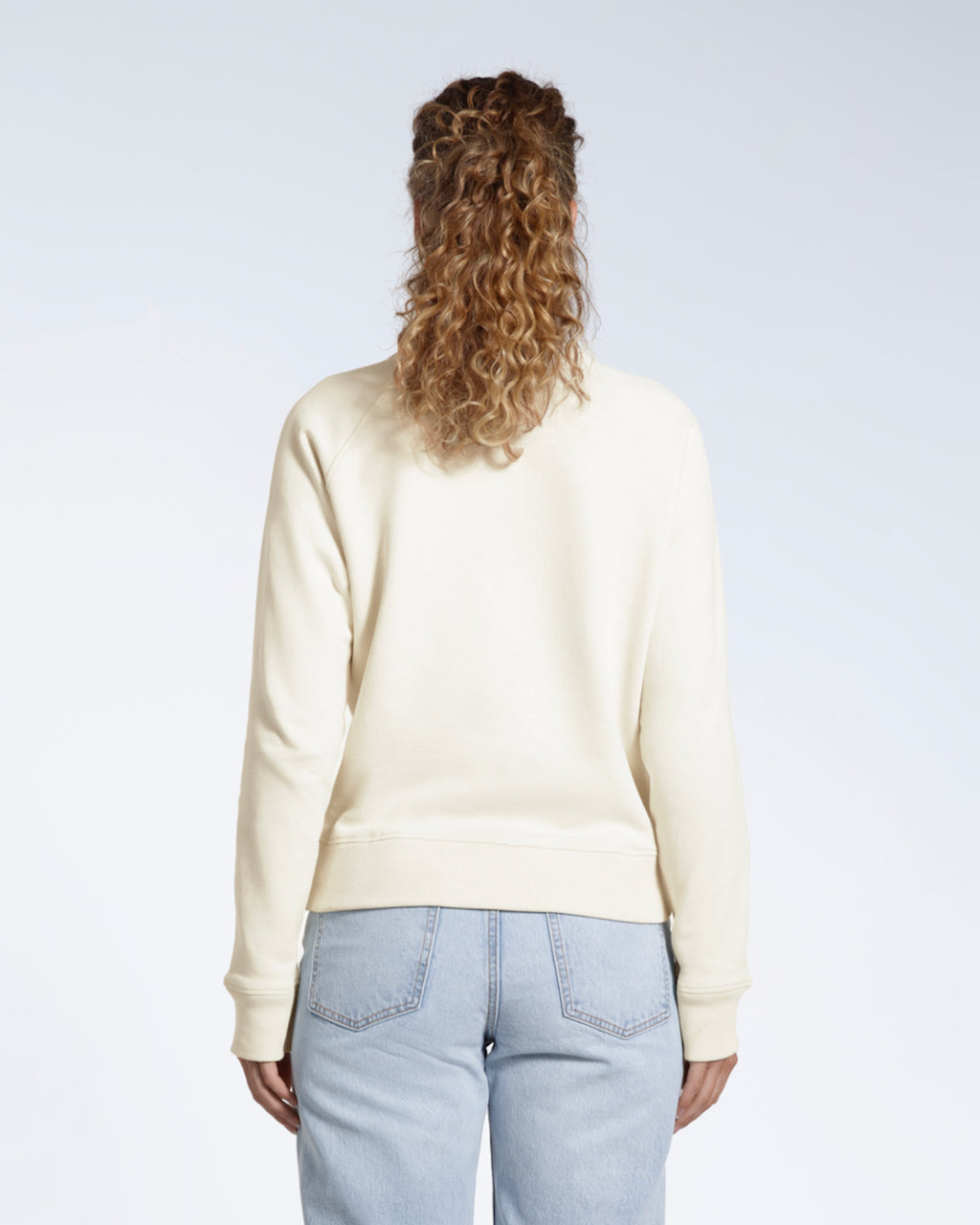 A woman facing away from the camera, showing the back of her plain ecru french terry organic cotton sweatshirt.
