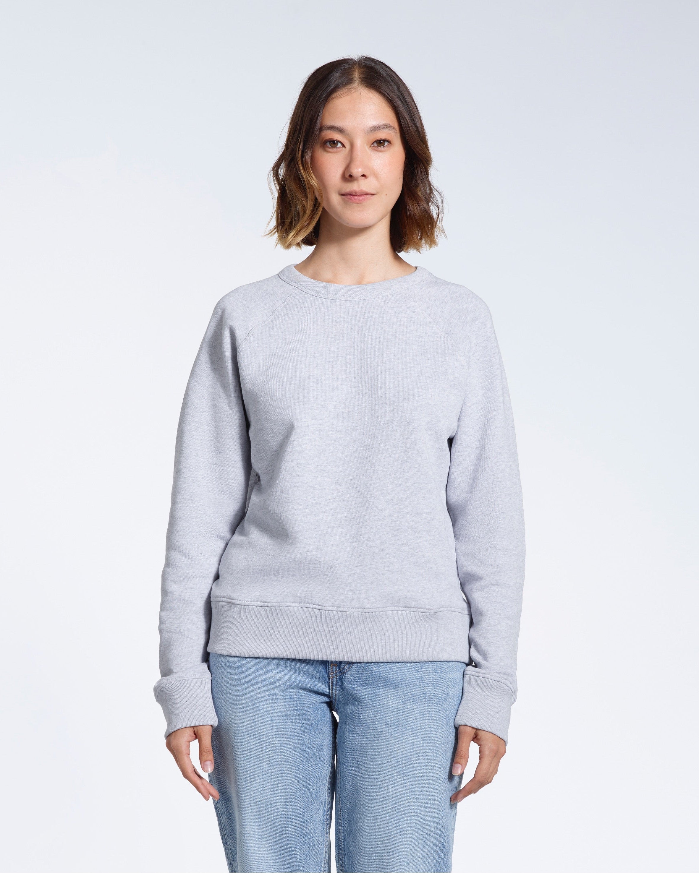 A woman face on looking into the camera with her arms by her side, modelling a plain grey french terry organic cotton sweatshirt.