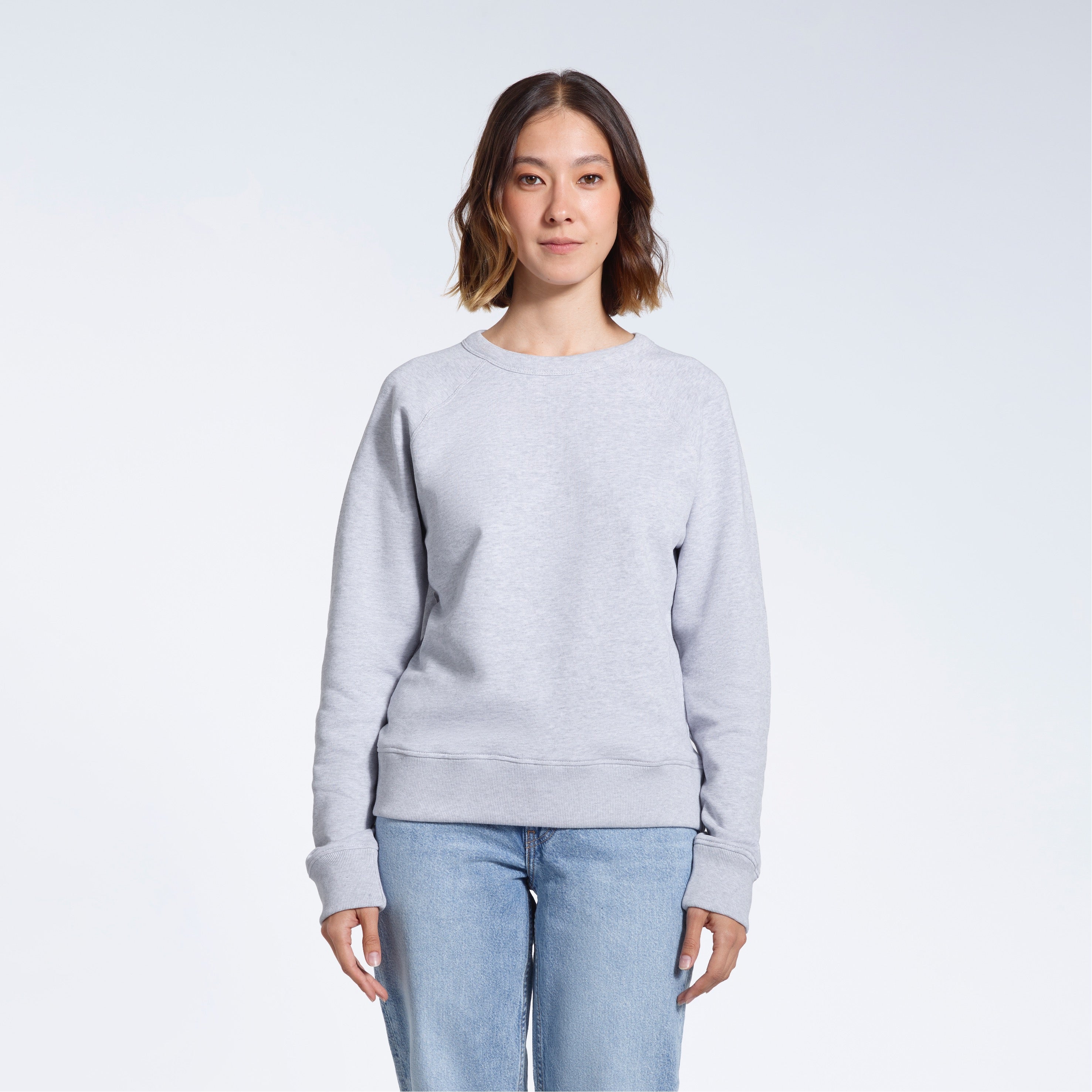 A woman face on looking into the camera with her arms by her side, modelling a plain grey french terry organic cotton sweatshirt.
