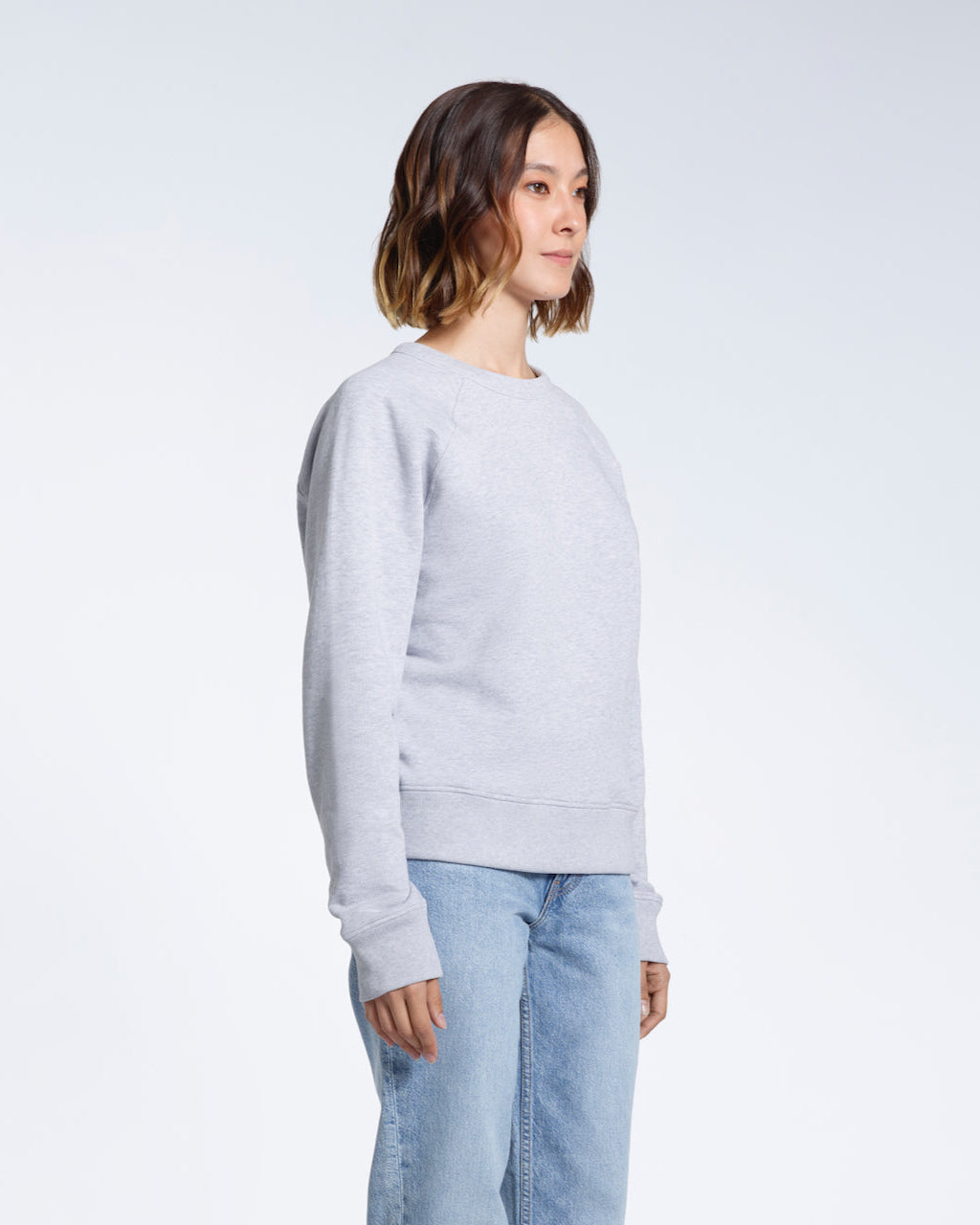 A woman looking away from the camera with her arms by her side, modelling a plain grey french terry organic cotton sweatshirt.