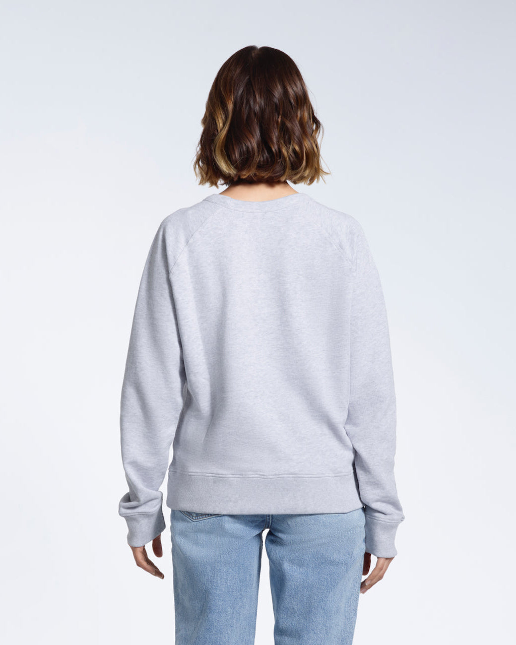 A woman facing away from the camera, showing the back of her plain grey french terry organic cotton sweatshirt.