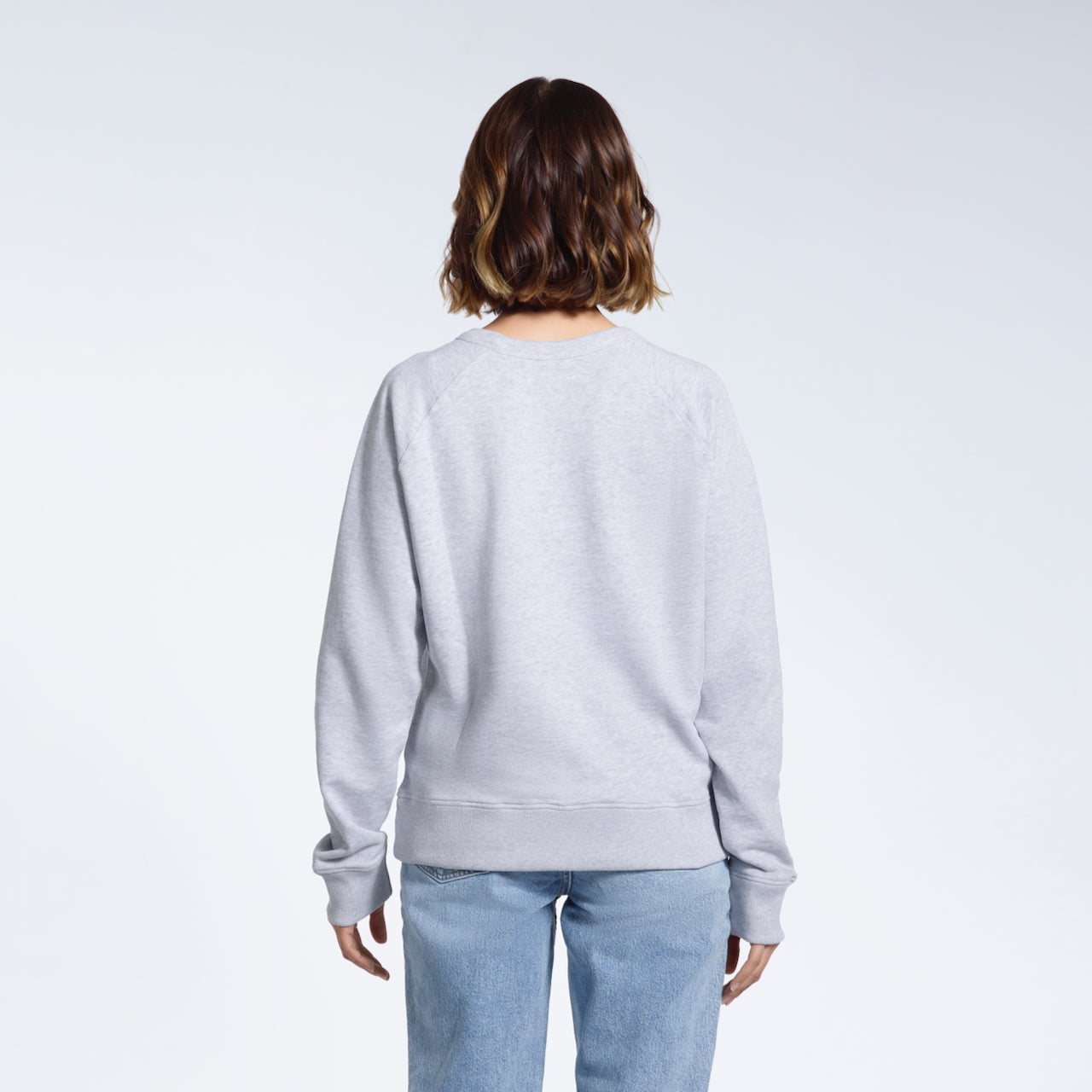A woman facing away from the camera, showing the back of her plain grey french terry organic cotton sweatshirt.