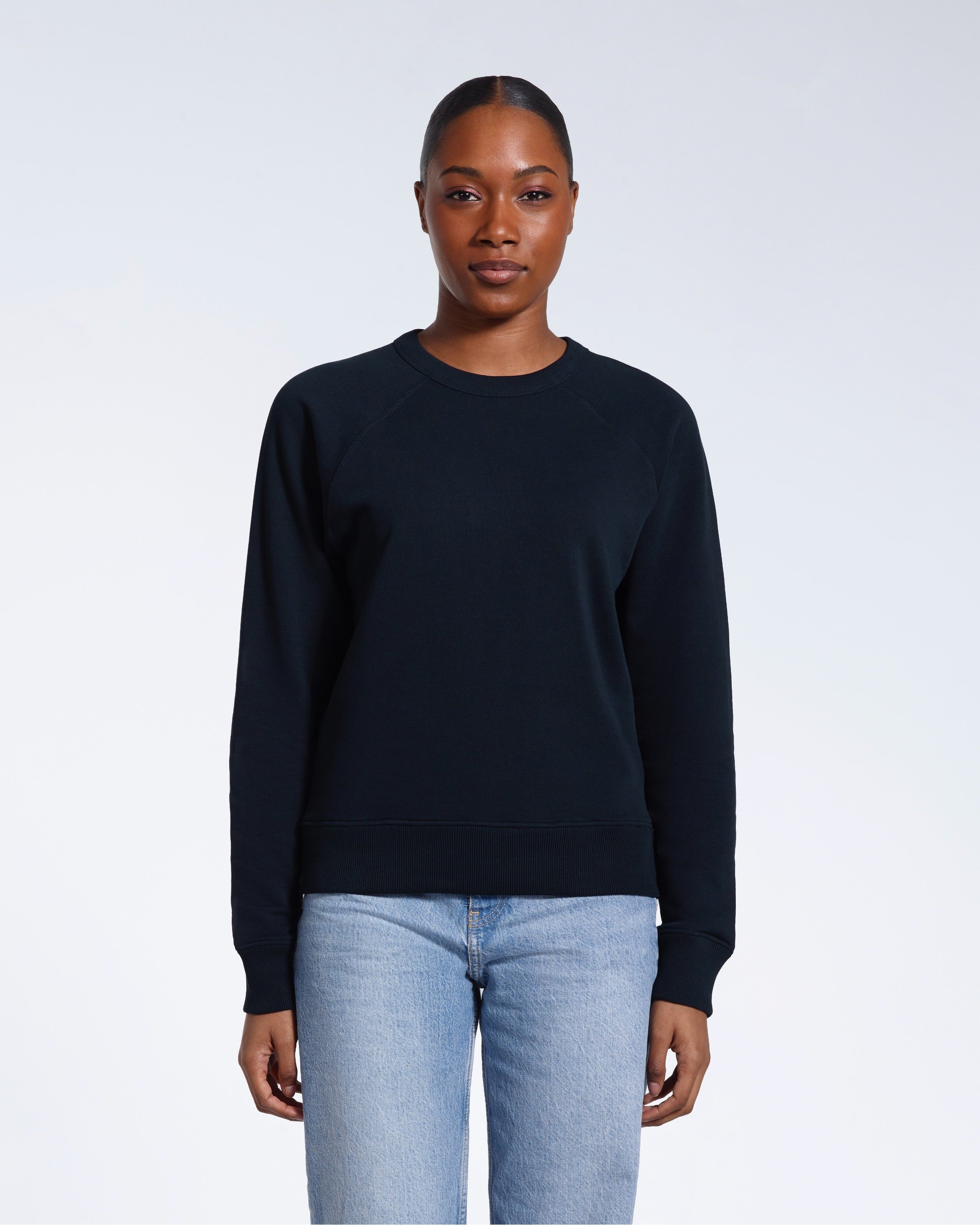 A woman face on looking into the camera with her arms by her side, modelling a plain navy french terry organic cotton sweatshirt.