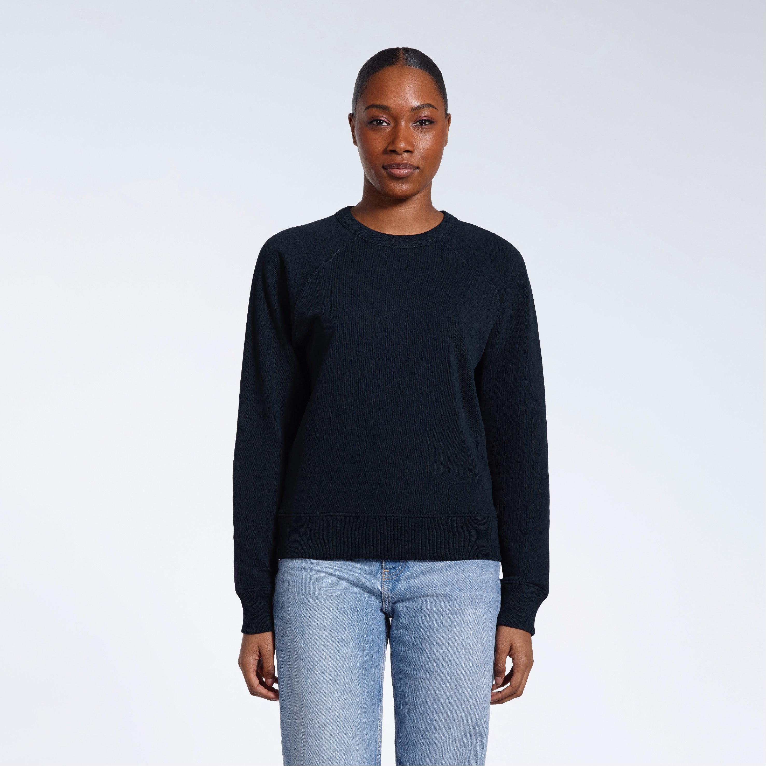 A woman face on looking into the camera with her arms by her side, modelling a plain navy french terry organic cotton sweatshirt.