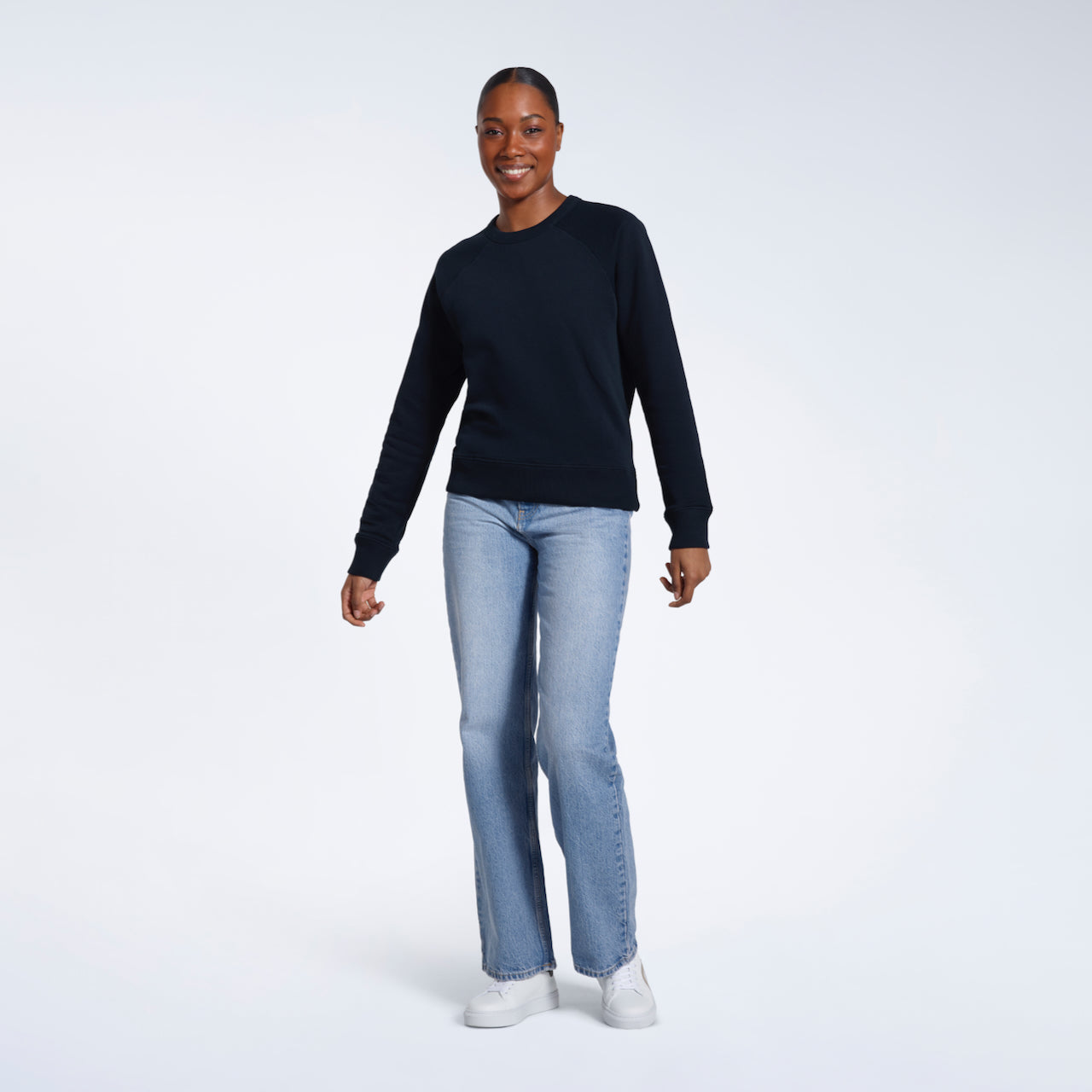 A full body photo of a woman smiling into the camera, modelling a plain navy french terry organic cotton sweatshirt.