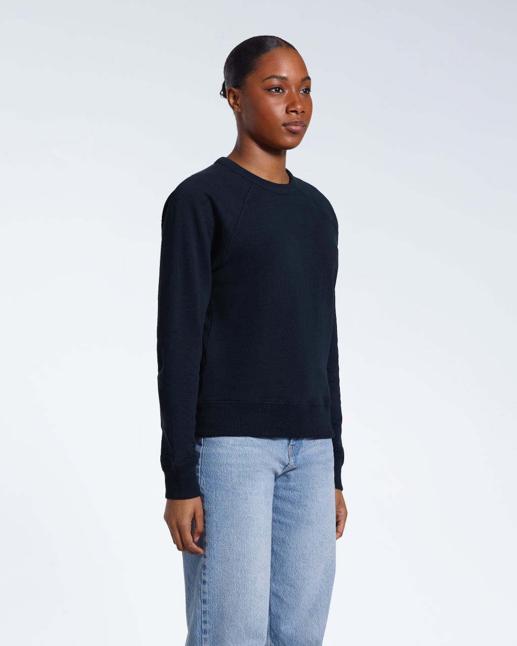 A woman looking away from the camera with her arms by her side, modelling a plain navy french terry organic cotton sweatshirt.