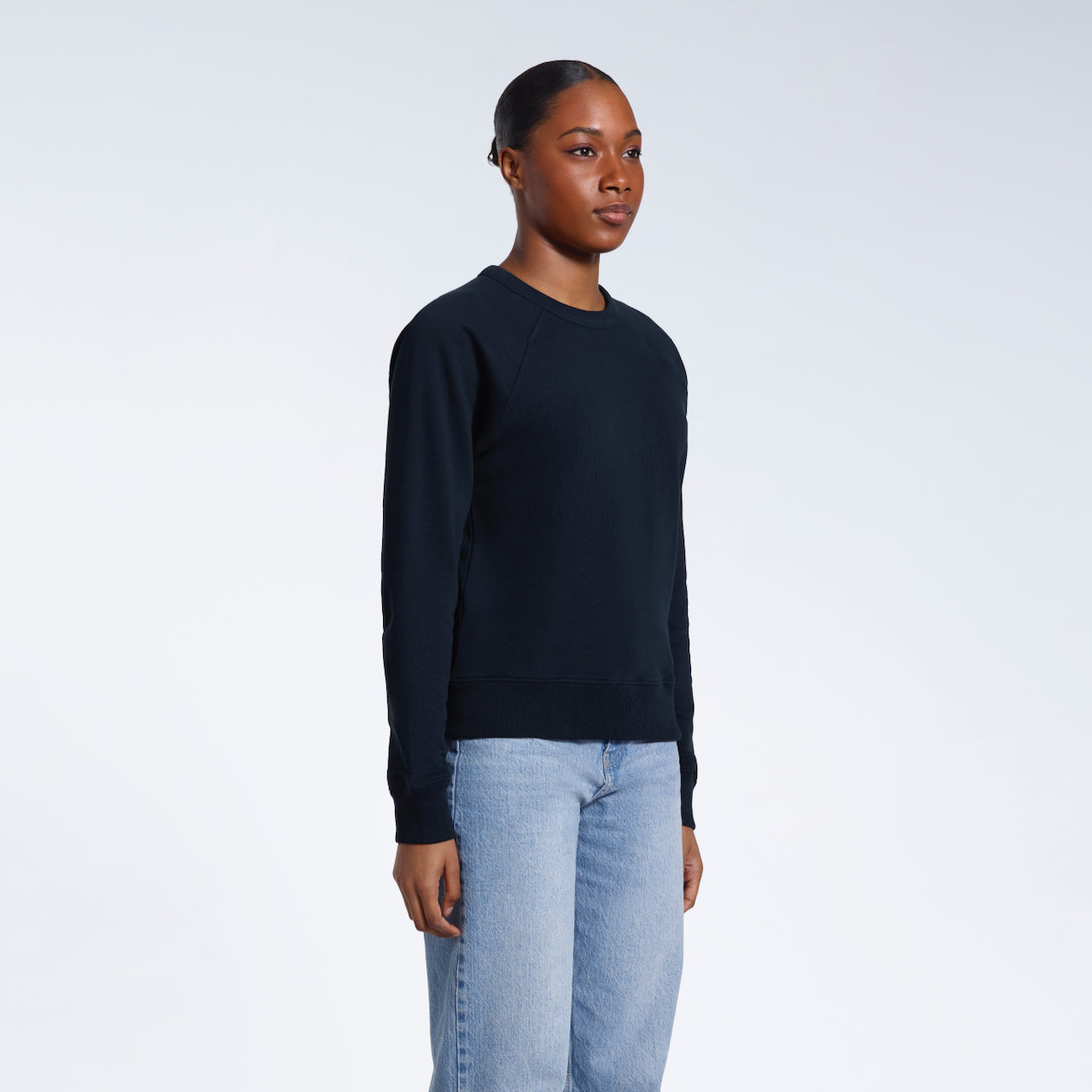 A woman looking away from the camera with her arms by her side, modelling a plain navy french terry organic cotton sweatshirt.