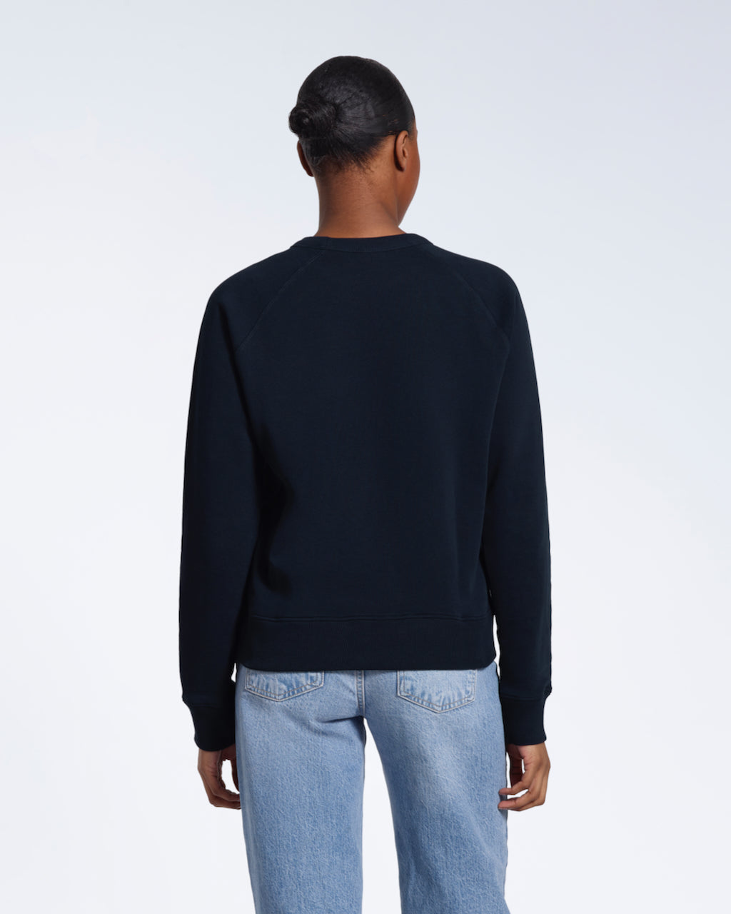 A woman facing away from the camera, showing the back of her plain navy french terry organic cotton sweatshirt.