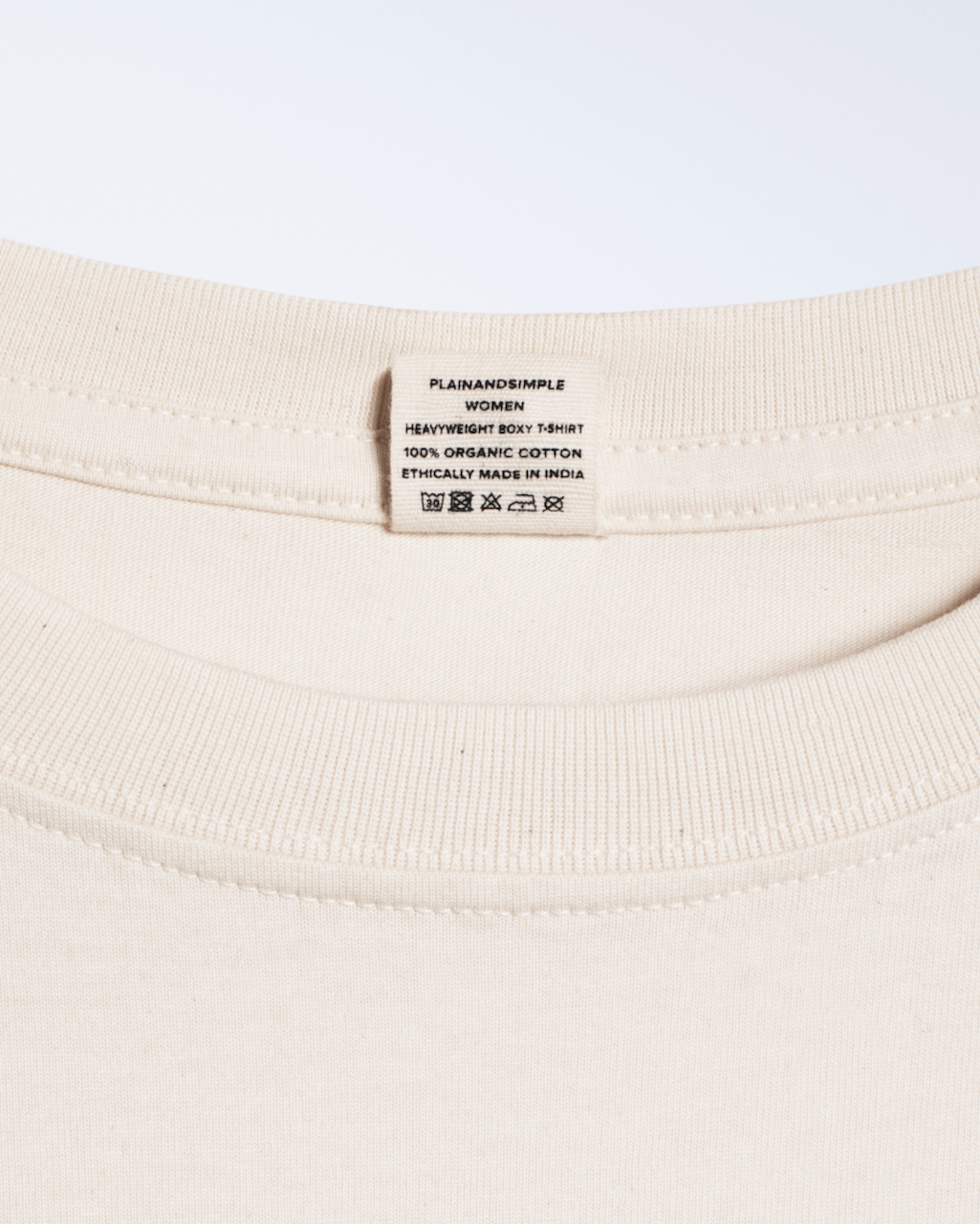 A close up of the neck label in a natural coloured, heavyweight, boxy organic cotton t shirt.