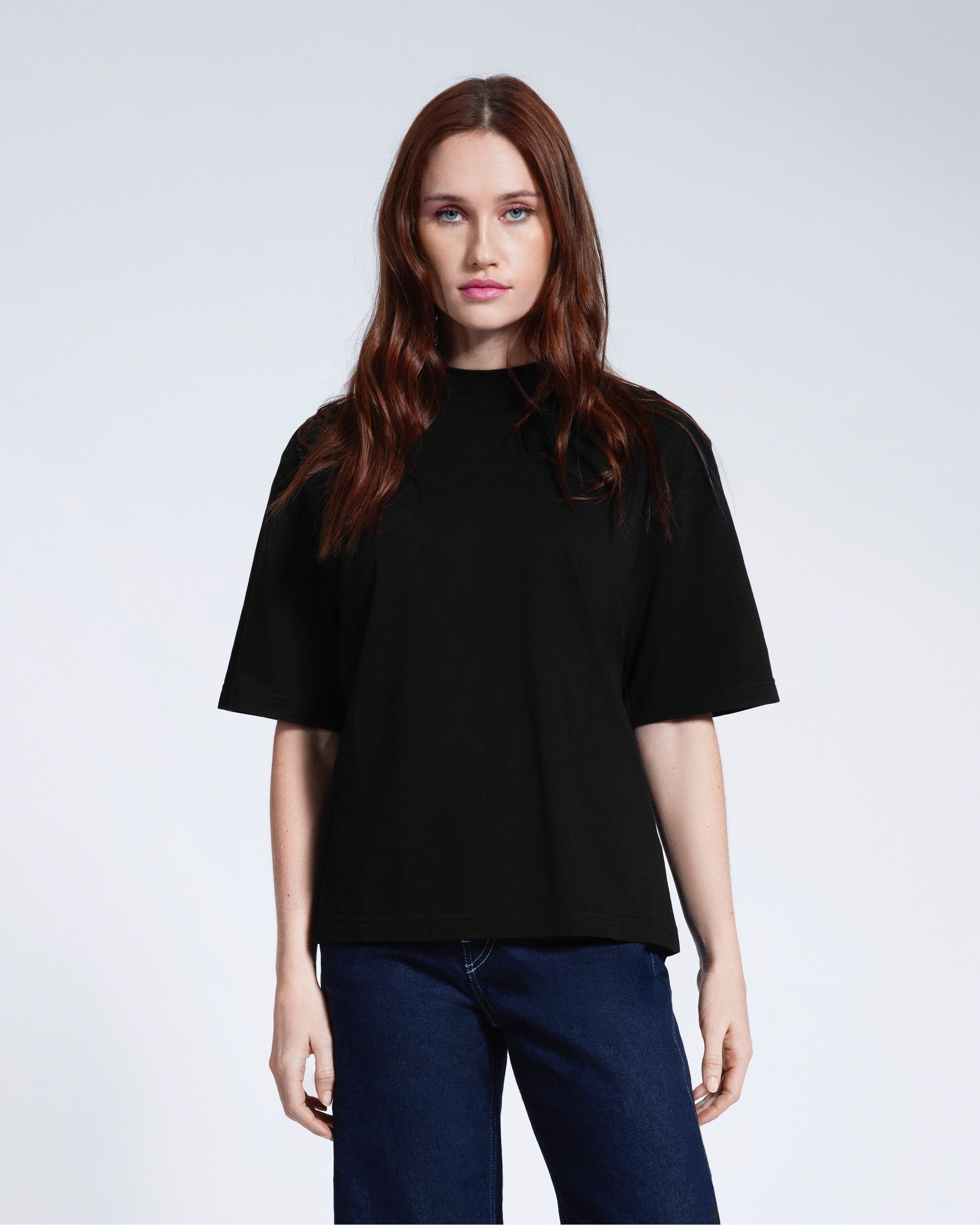 A woman face on looking into the camera, modelling a plain black boxy heavyweight organic cotton t shirt.