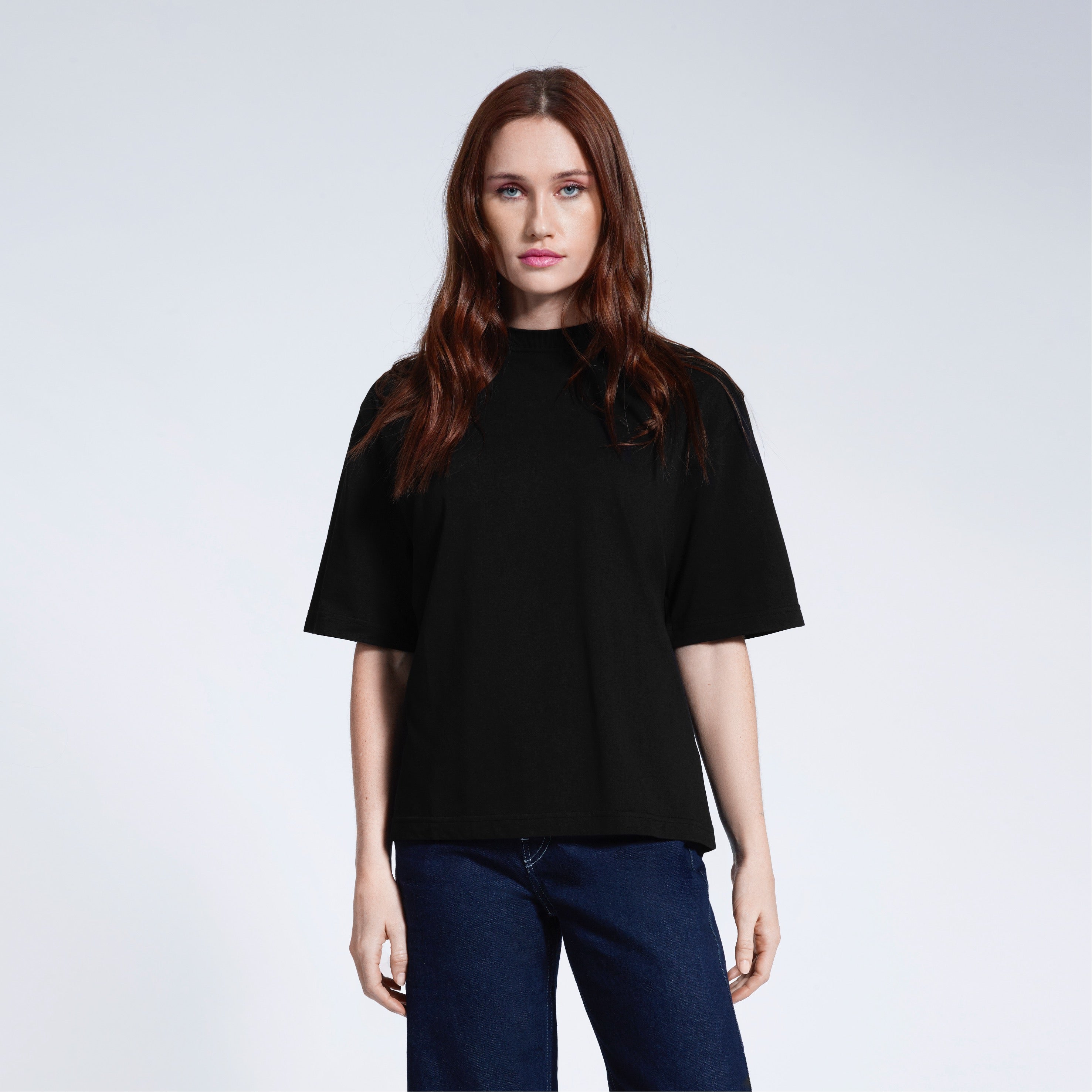 A woman face on looking into the camera, modelling a plain black boxy heavyweight organic cotton t shirt.