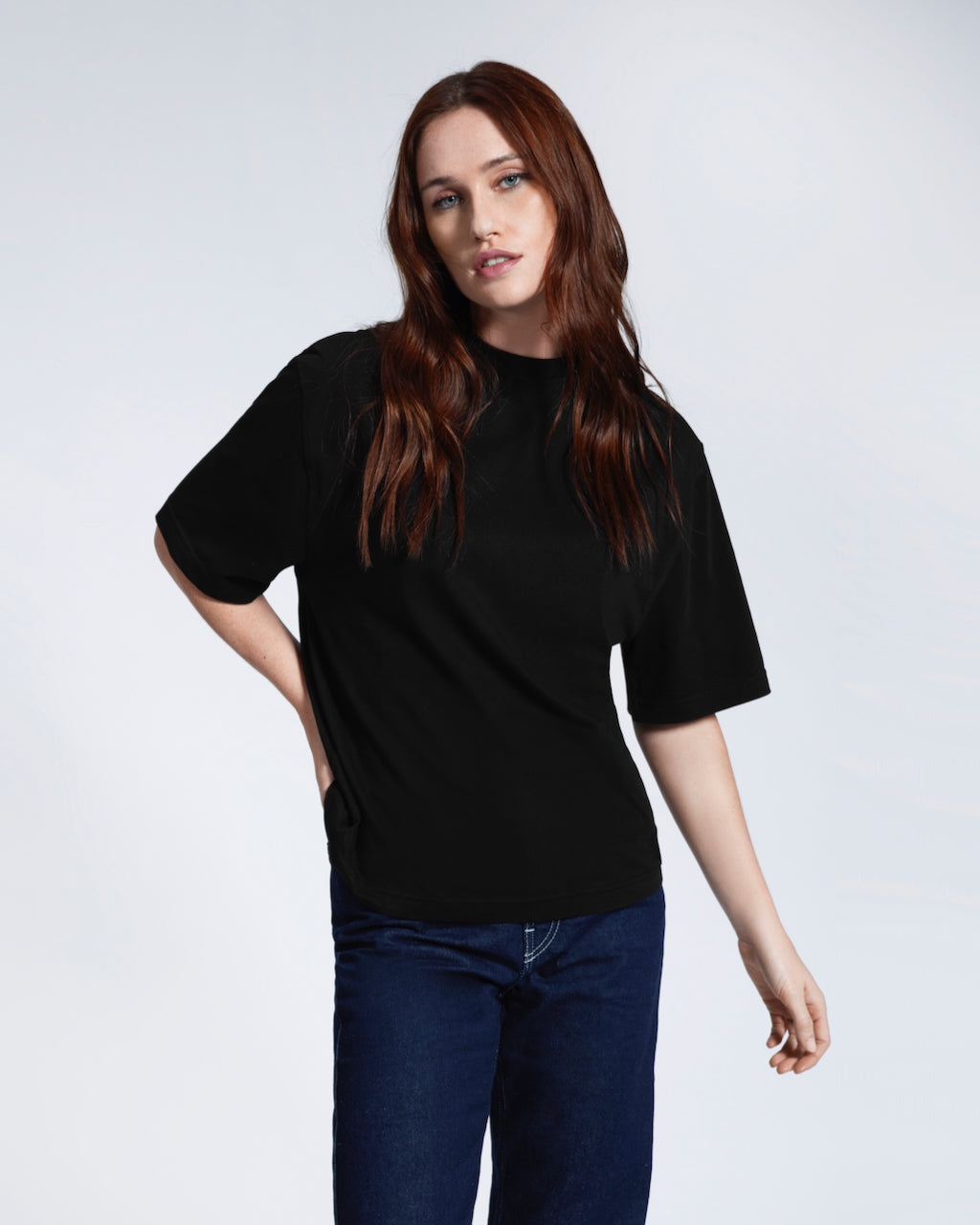 A woman with her hand by her hip looking into the camera, modelling a plain black boxy heavyweight organic cotton t shirt.