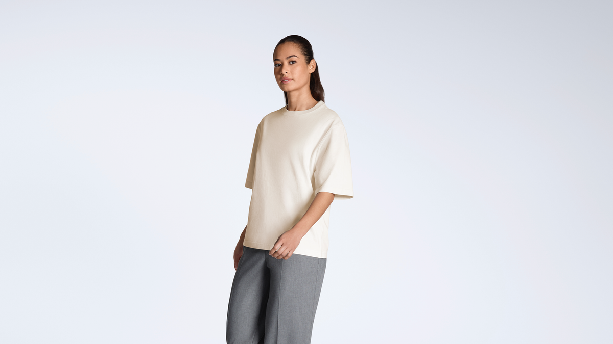 A woman looking into the camera, modelling a plain natural coloured, boxy, heavyweight, organic cotton t shirt.