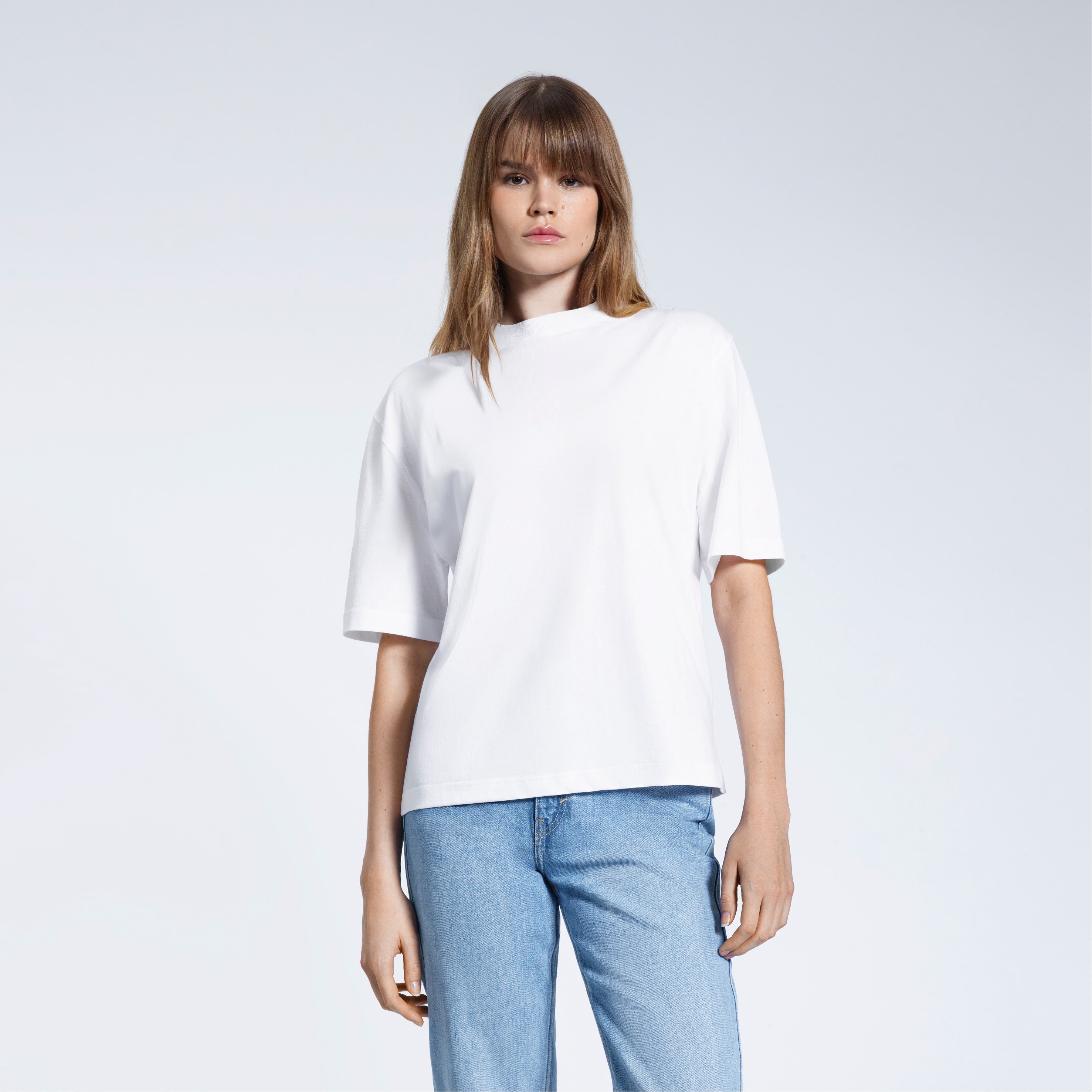 A woman face on looking into the camera, modelling a plain white boxy heavyweight organic cotton t shirt.