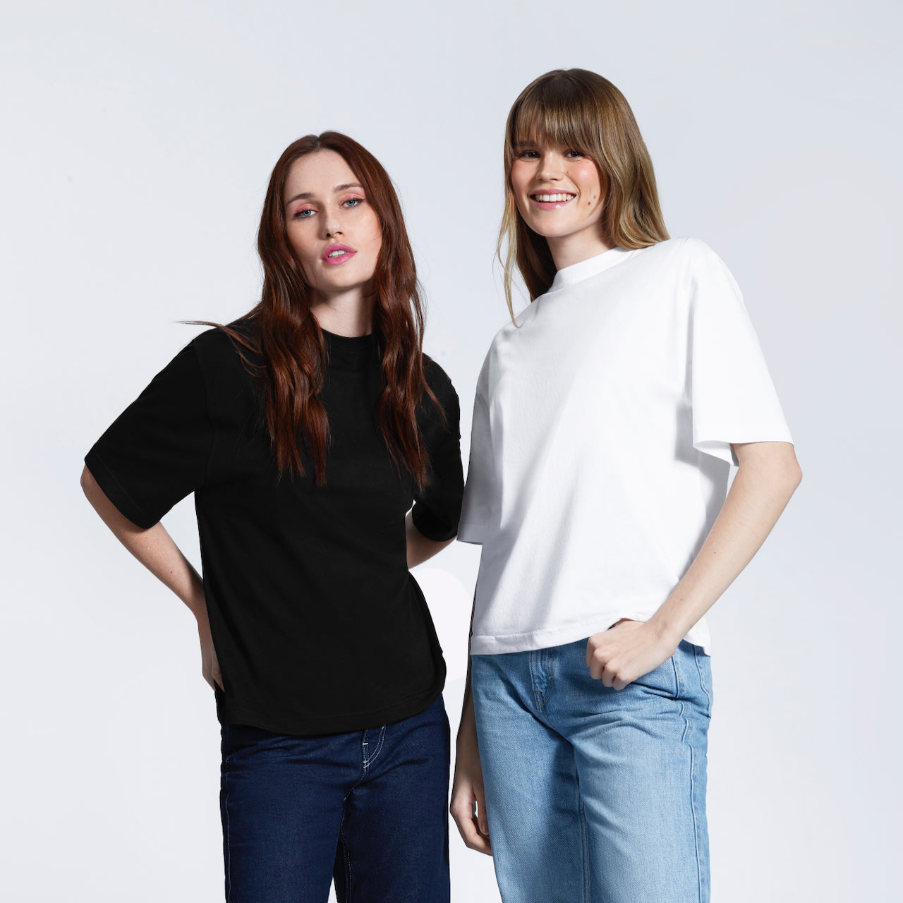 Two women looking at the camera, modelling heavyweight organic cotton boxy, oversized plain white and black short sleeve t shirts.