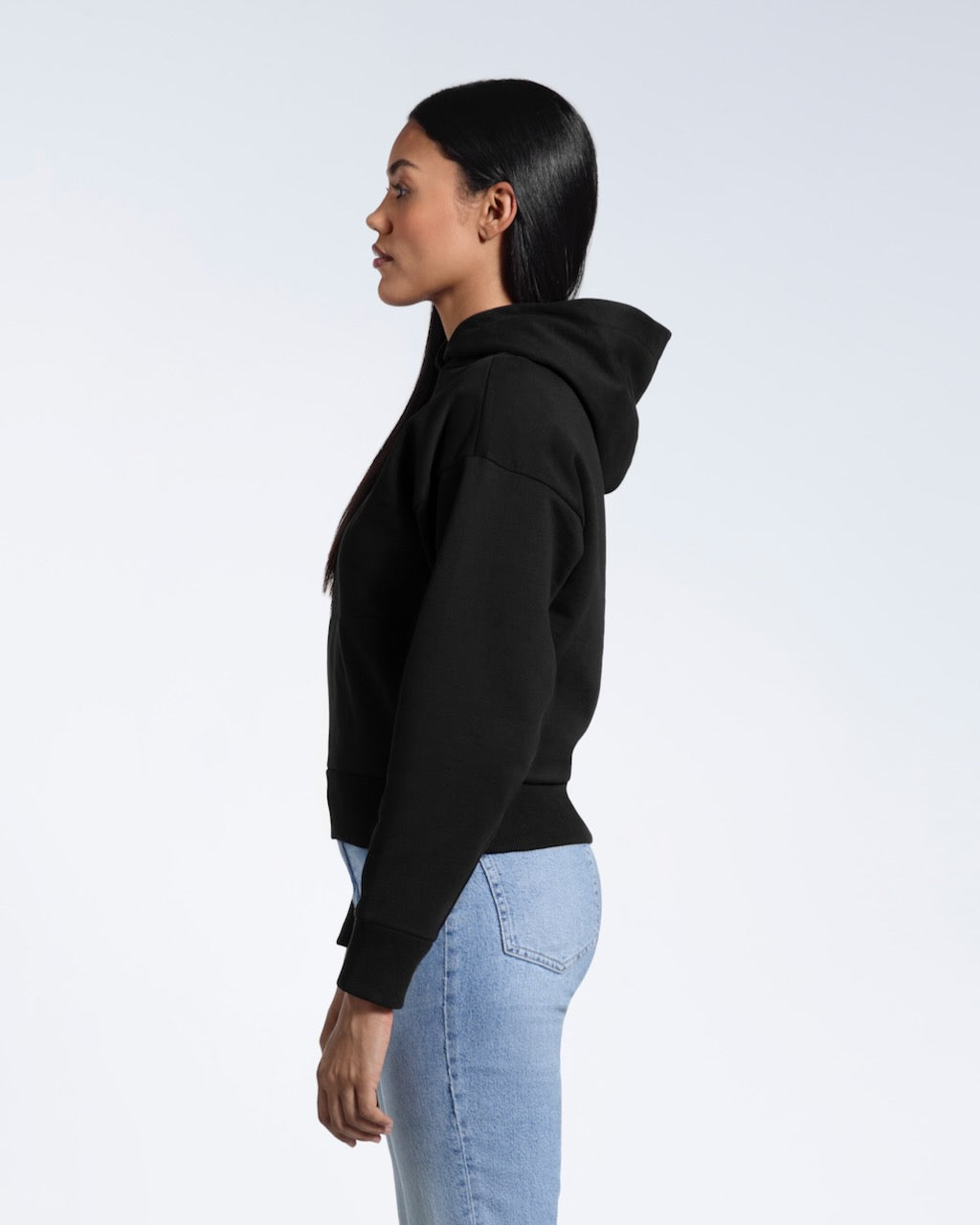 A woman facing side on, modelling a black heavyweight organic cotton hoodie.