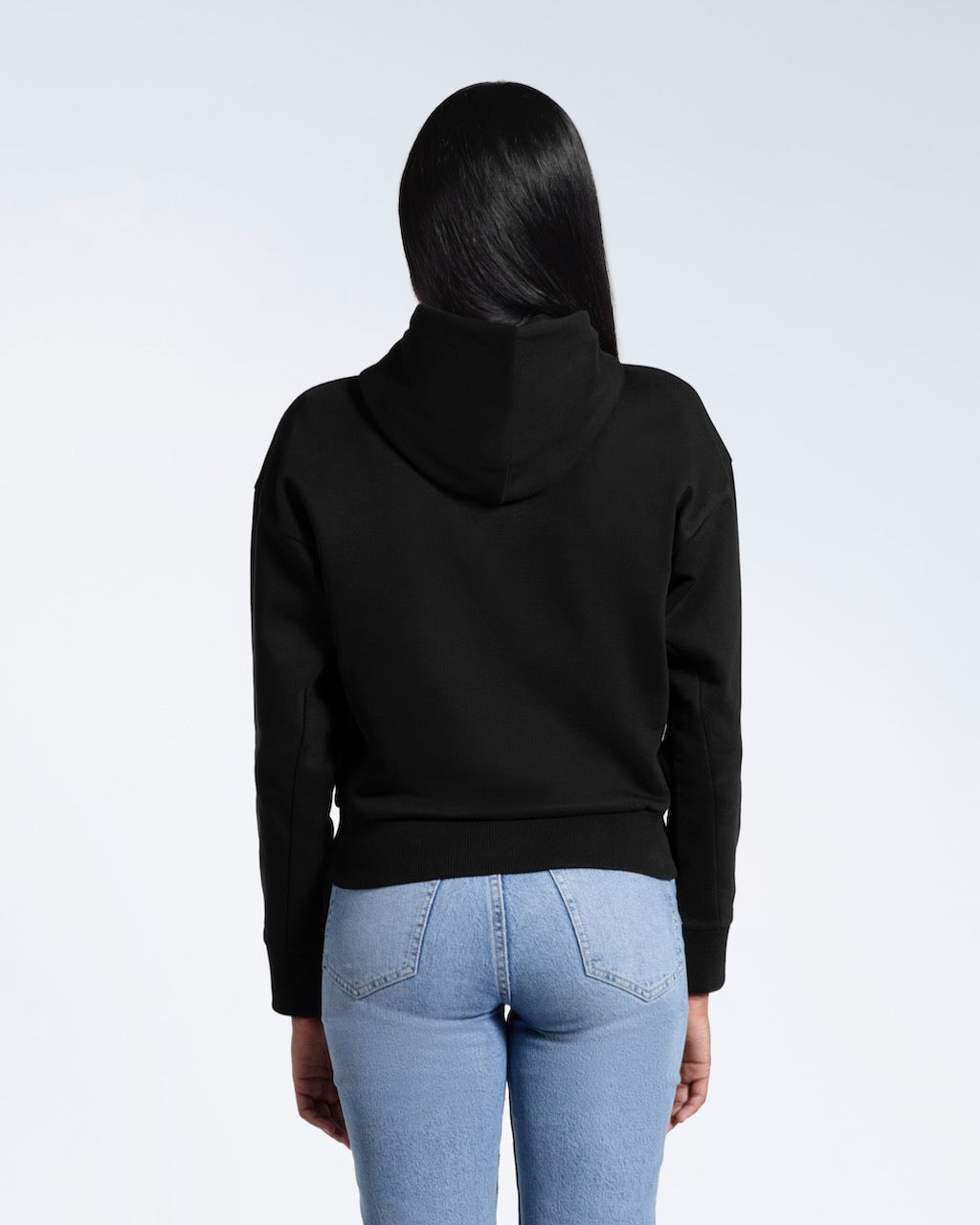 A woman facing away from the camera with her arms by her sides, modelling a black heavyweight organic cotton hoodie.