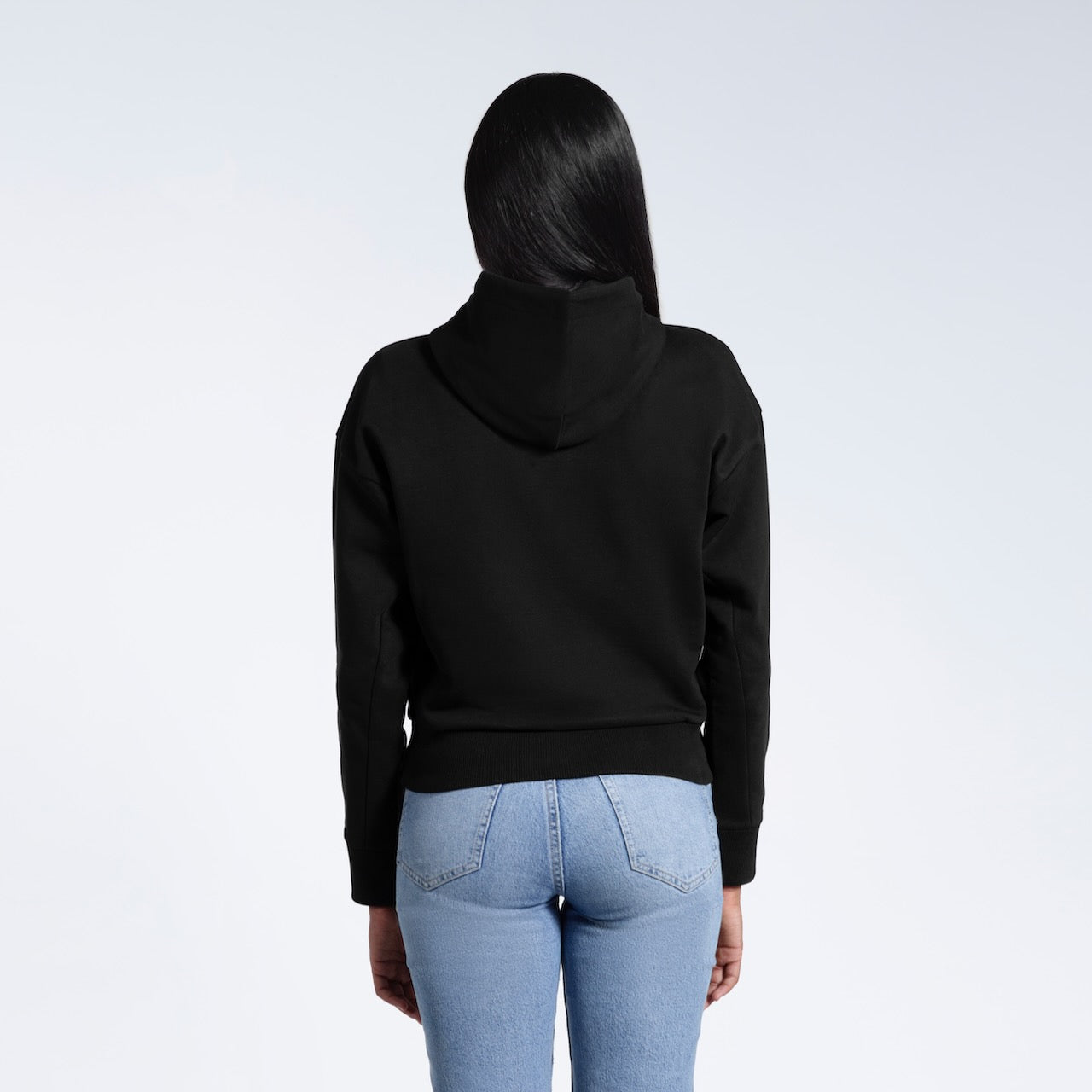 A woman facing away from the camera with her arms by her sides, modelling a black heavyweight organic cotton hoodie.