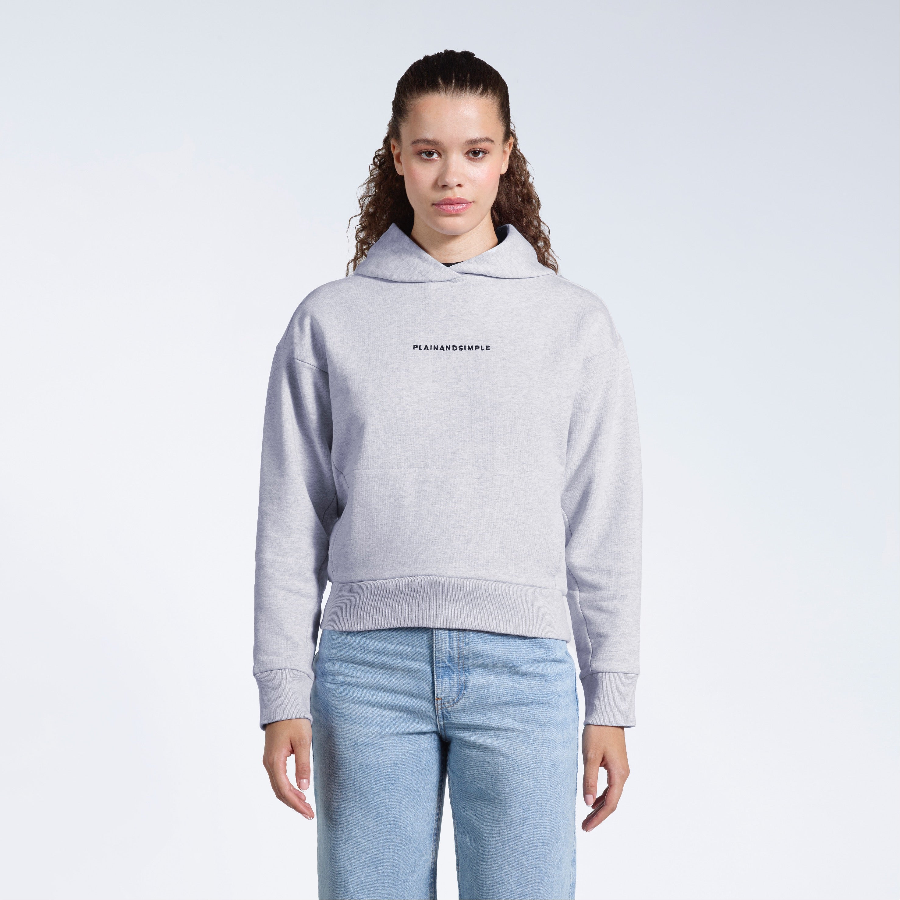 A woman facing front on looking into the camera with her arms by her sides, modelling a branded grey heavyweight organic cotton hoodie.