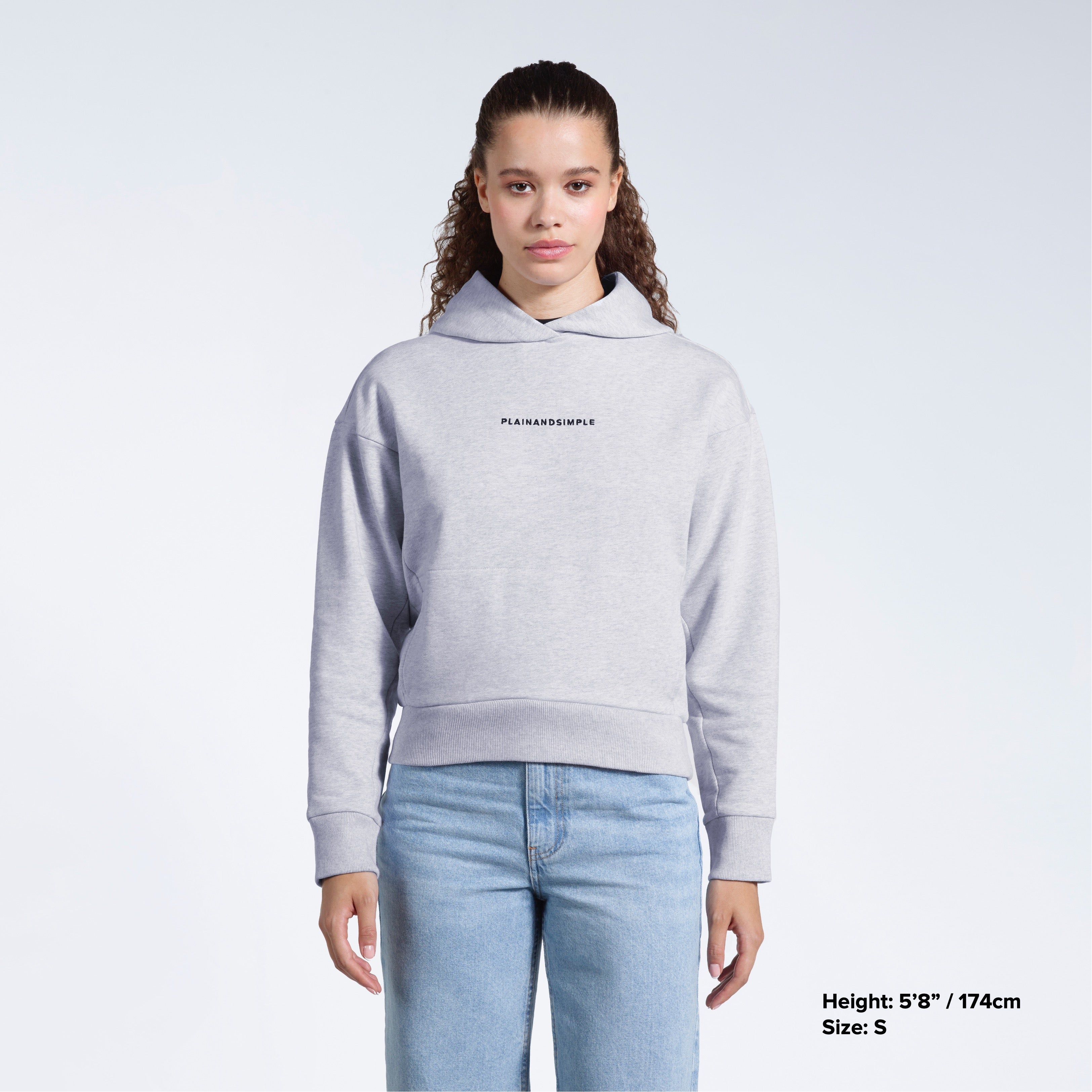 A woman facing front on looking into the camera with her arms by her sides, modelling a branded grey heavyweight organic cotton hoodie.
