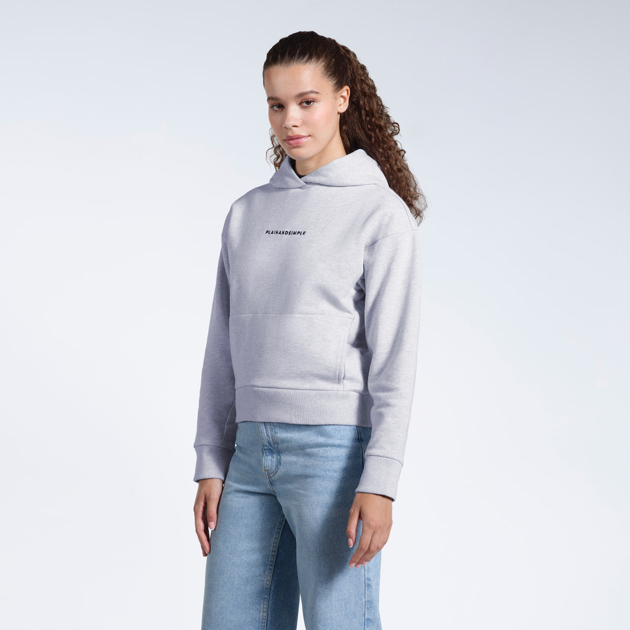 A woman at an angle looking into the camera, modelling a branded grey heavyweight organic cotton hoodie.