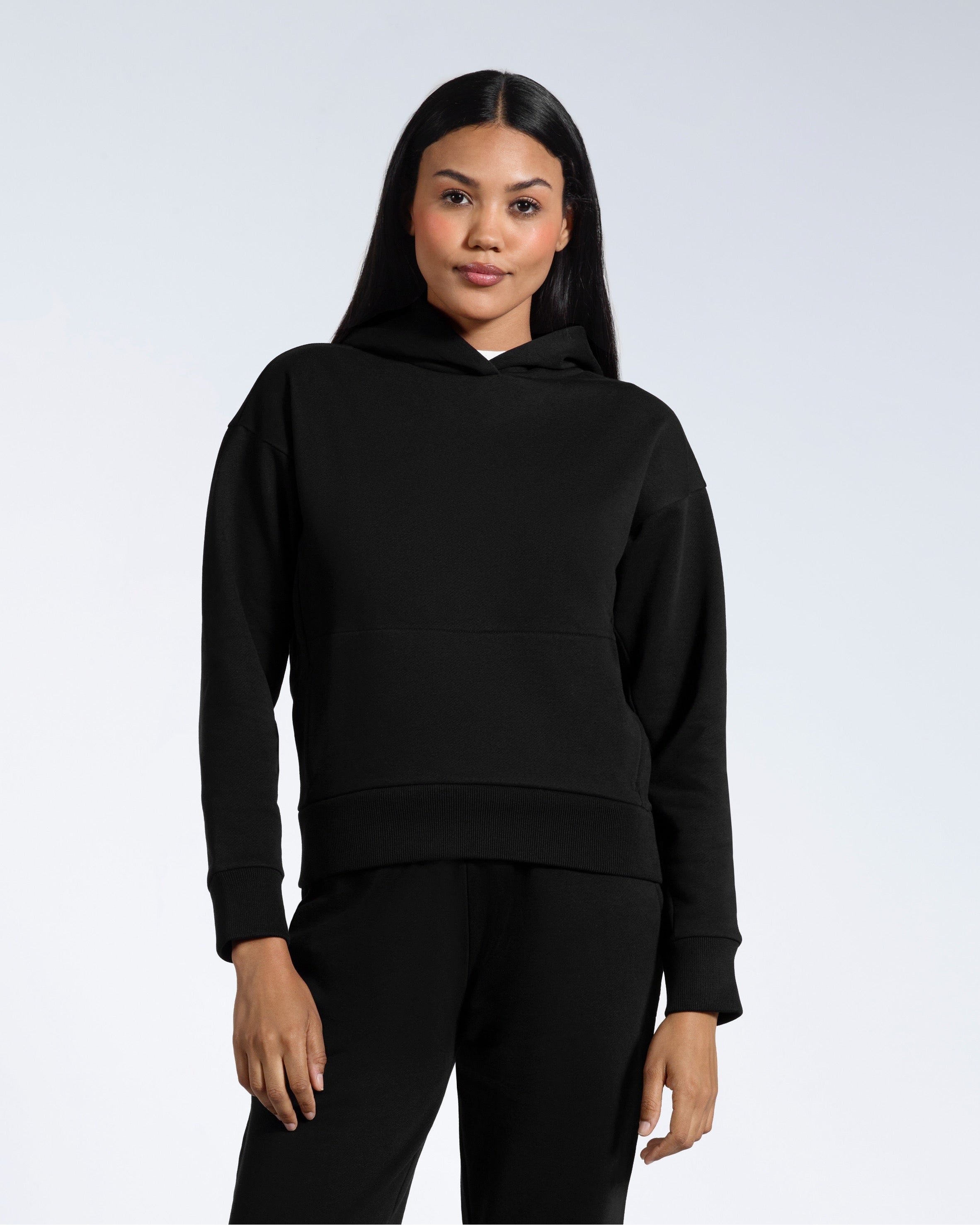 A woman facing front on looking into the camera with her arms by her sides, modelling a black heavyweight organic cotton hoodie.