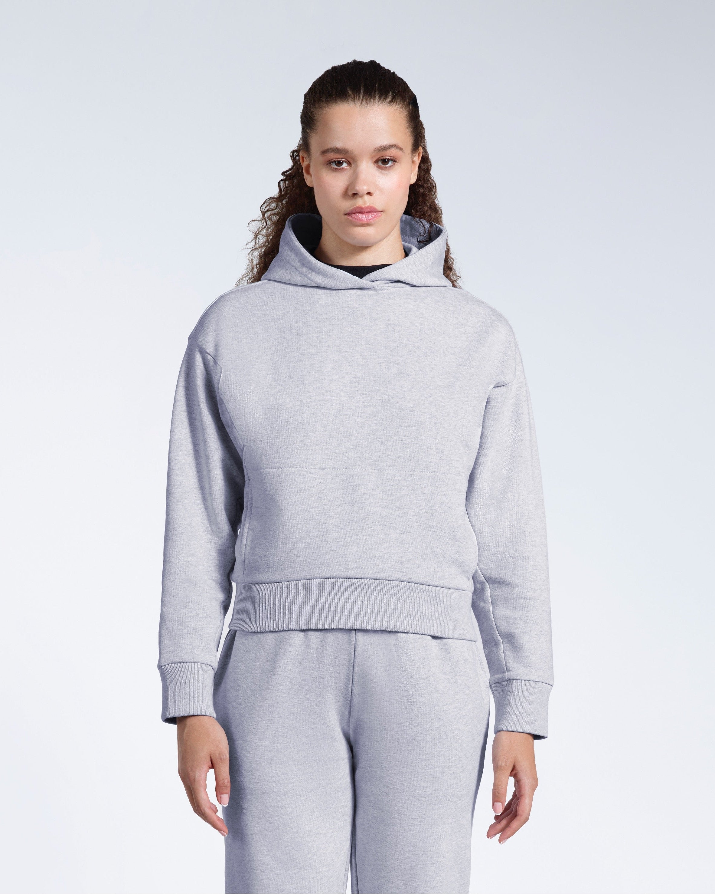 A woman facing front on looking into the camera with her arms by her sides, modelling a grey heavyweight organic cotton hoodie with matching joggers.