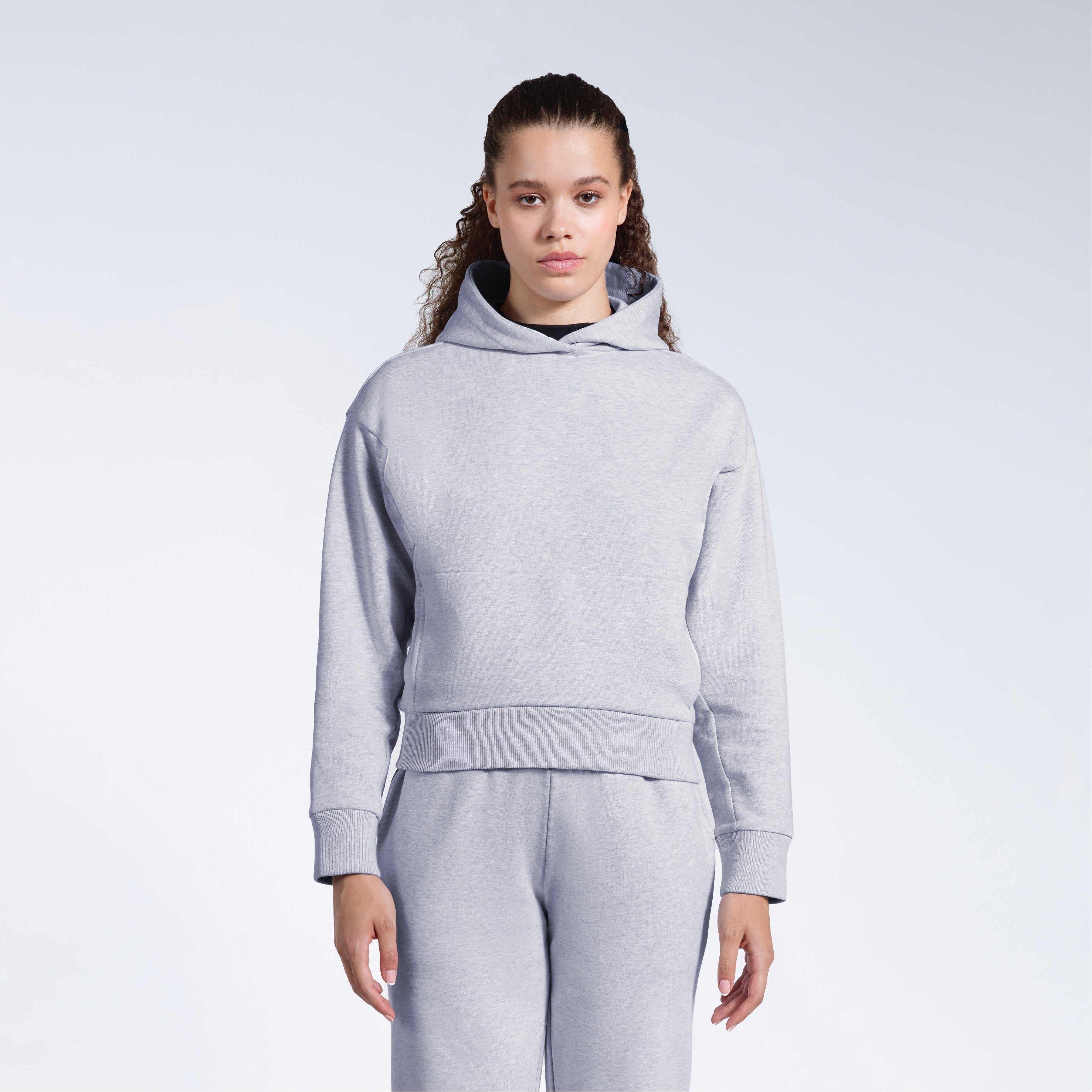 A woman facing front on looking into the camera with her arms by her sides, modelling a grey heavyweight organic cotton hoodie with matching joggers.