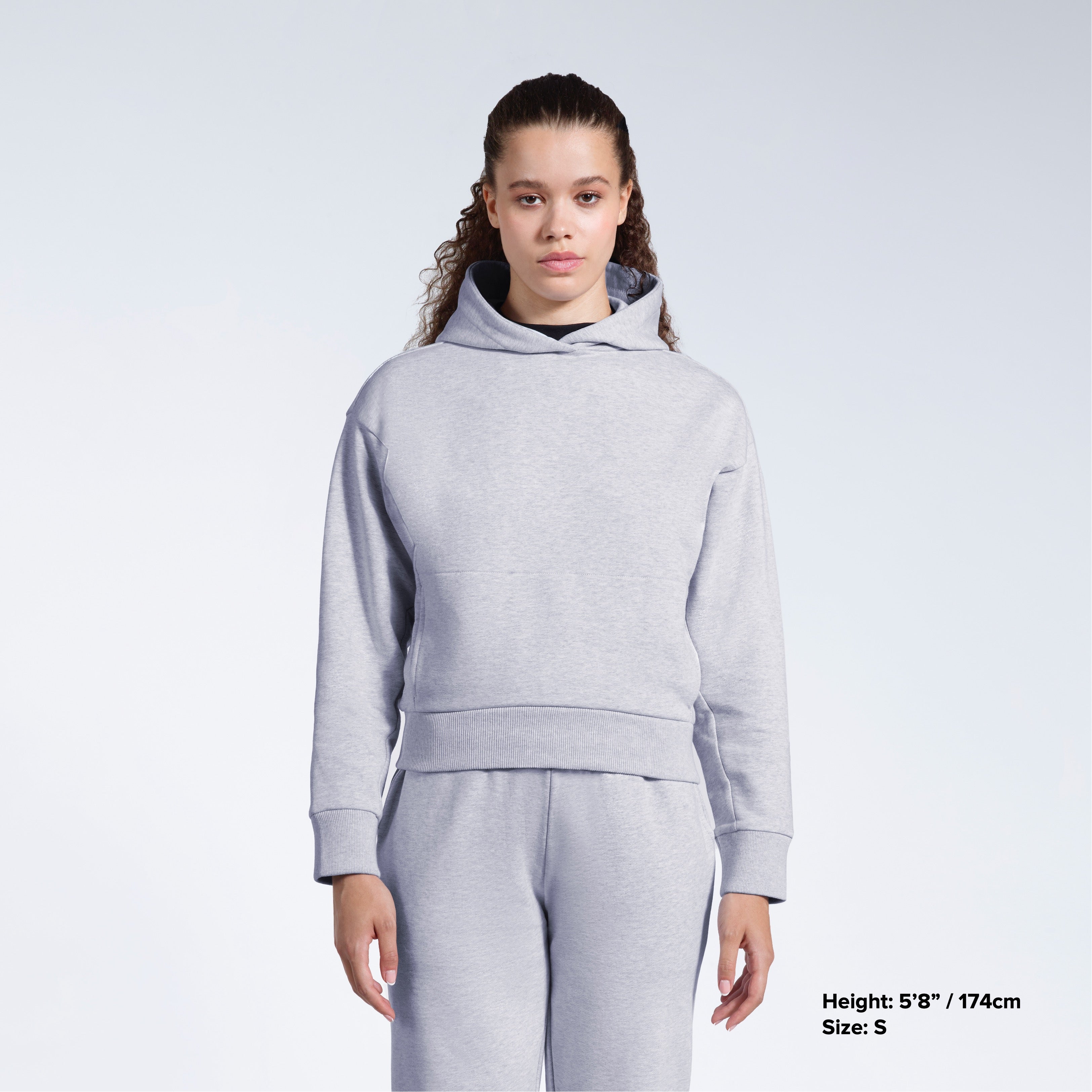 A woman facing front on looking into the camera with her arms by her sides, modelling a grey heavyweight organic cotton hoodie with matching joggers.