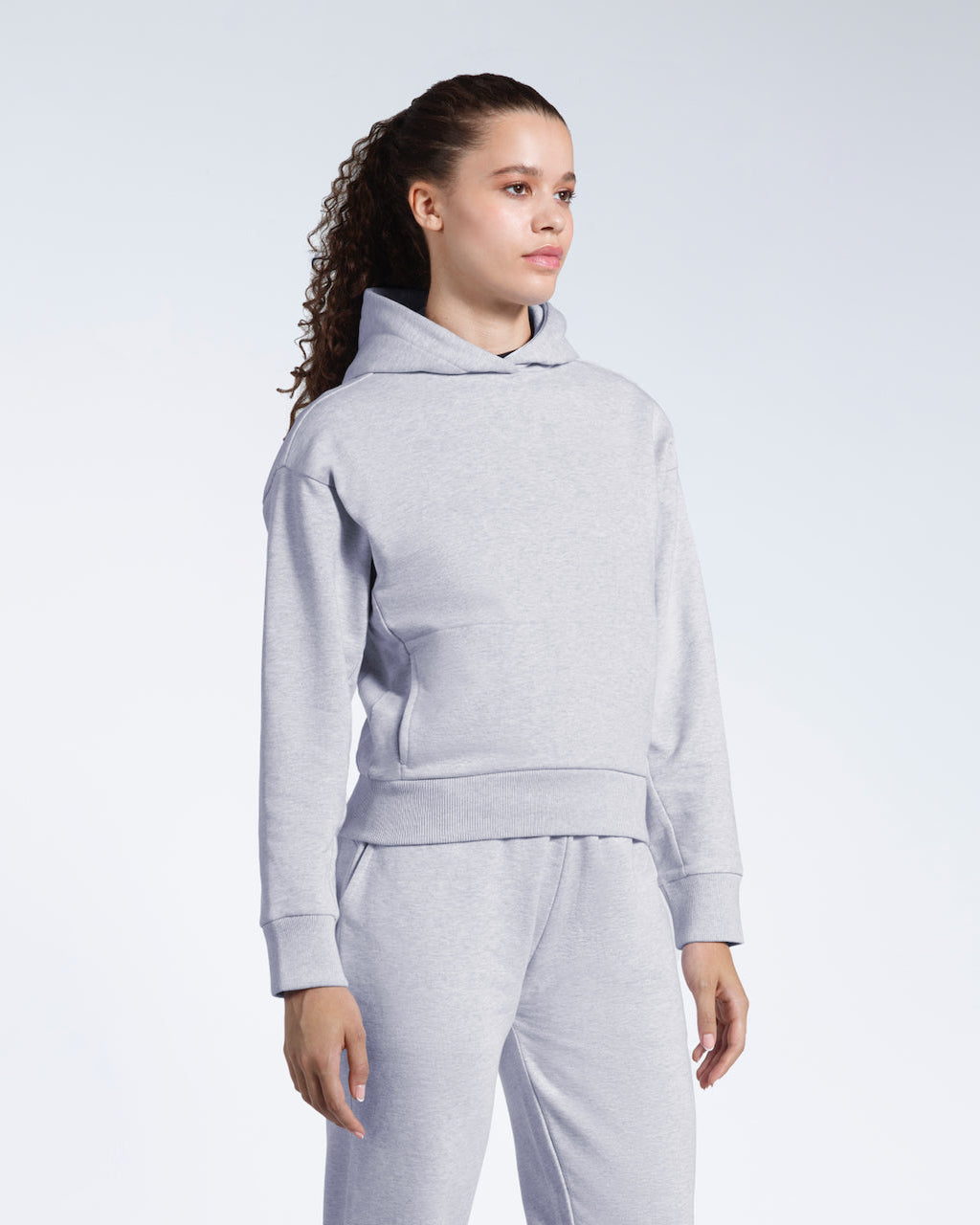 A woman looking away from the camera, modelling a grey heavyweight organic cotton hoodie with matching joggers.