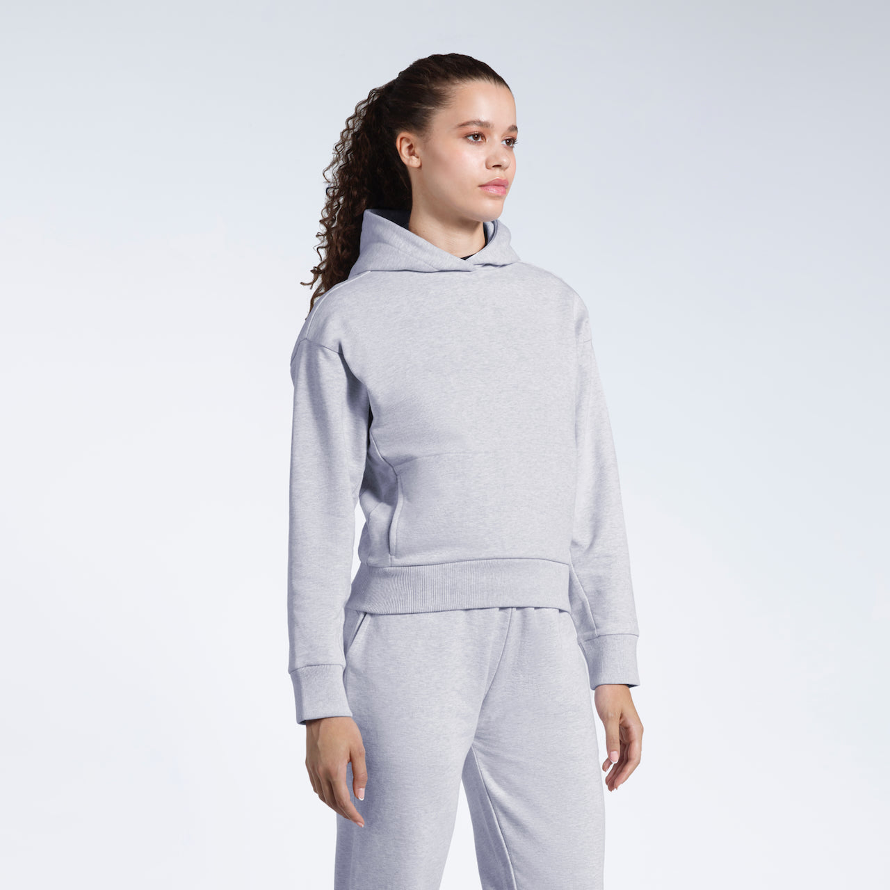 A woman looking away from the camera, modelling a grey heavyweight organic cotton hoodie with matching joggers.