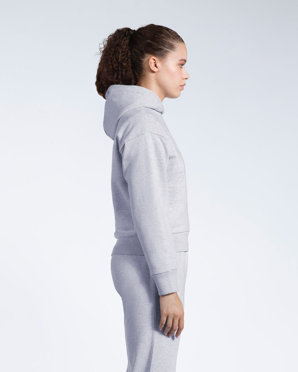 A woman facing side on, modelling a grey heavyweight organic cotton hoodie with matching joggers.