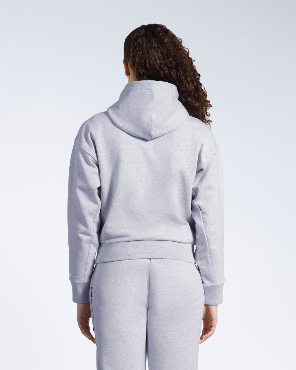 A woman facing away from the camera with her arms by her sides, modelling a grey heavyweight organic cotton hoodie with matching joggers.