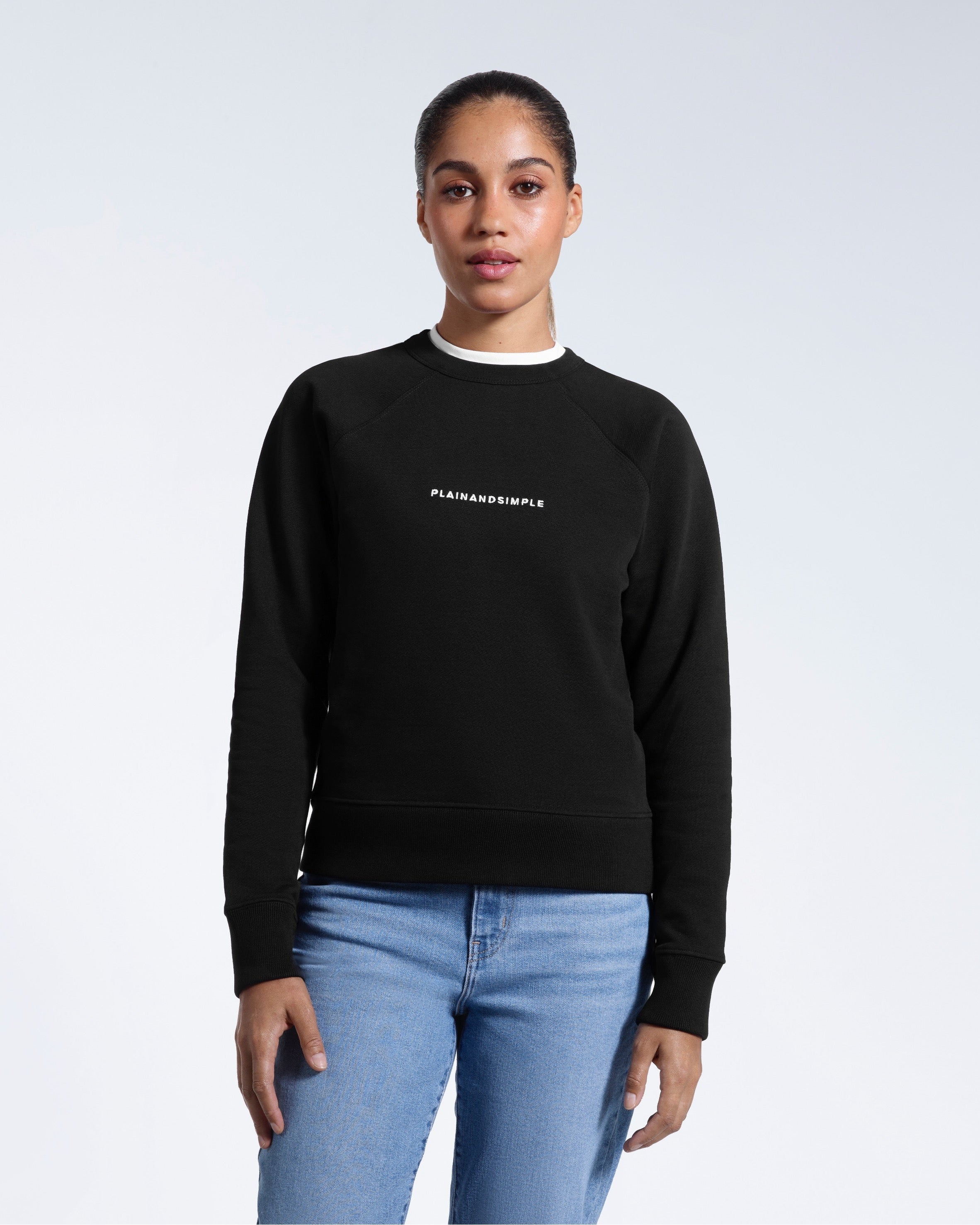 A woman face on with her arms by her side, modelling a branded black heavyweight organic cotton sweatshirt.